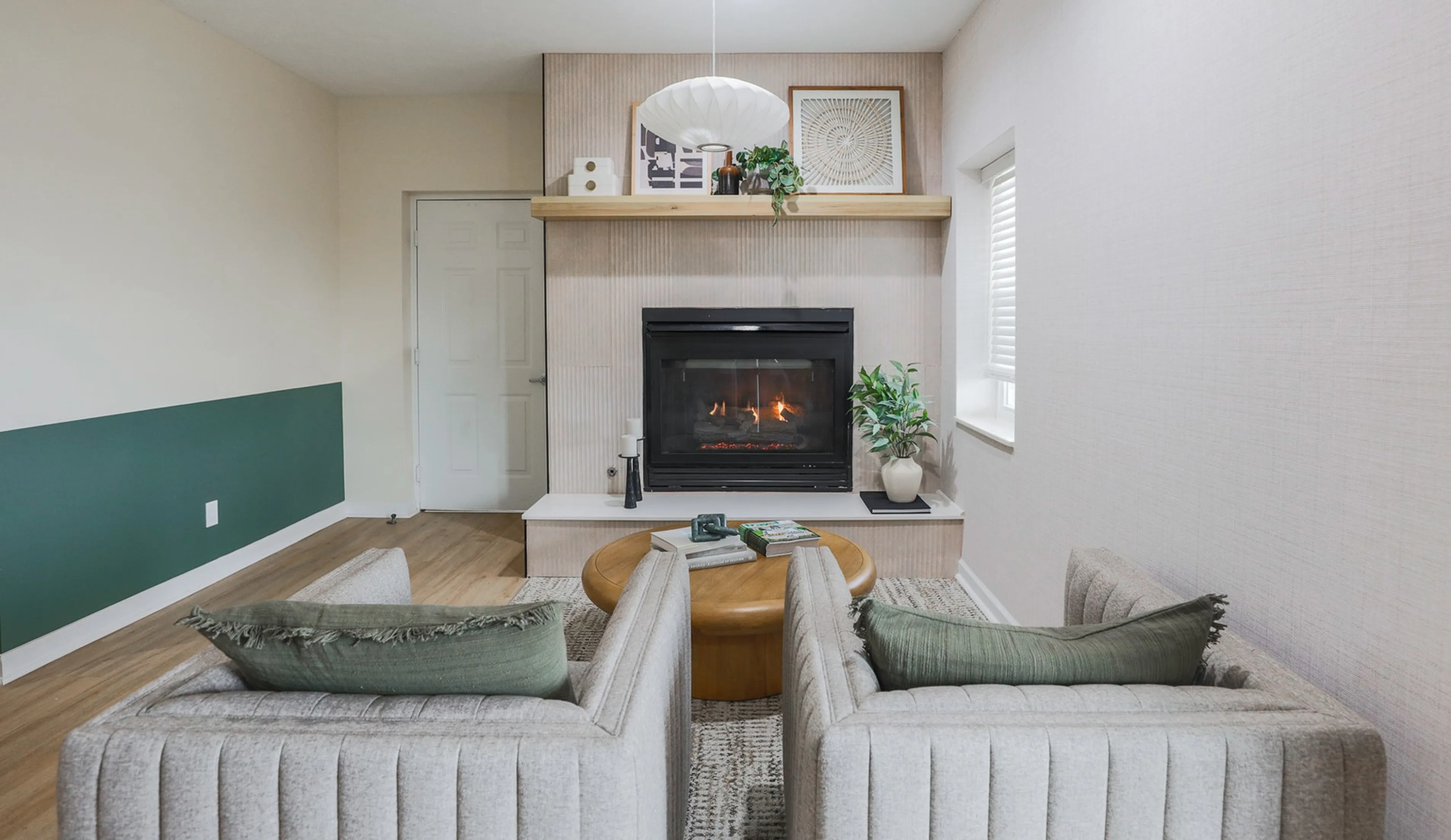 Cozy living room with elegant fireplace, stylish gray sofas with green cushions, and chic wooden accents.