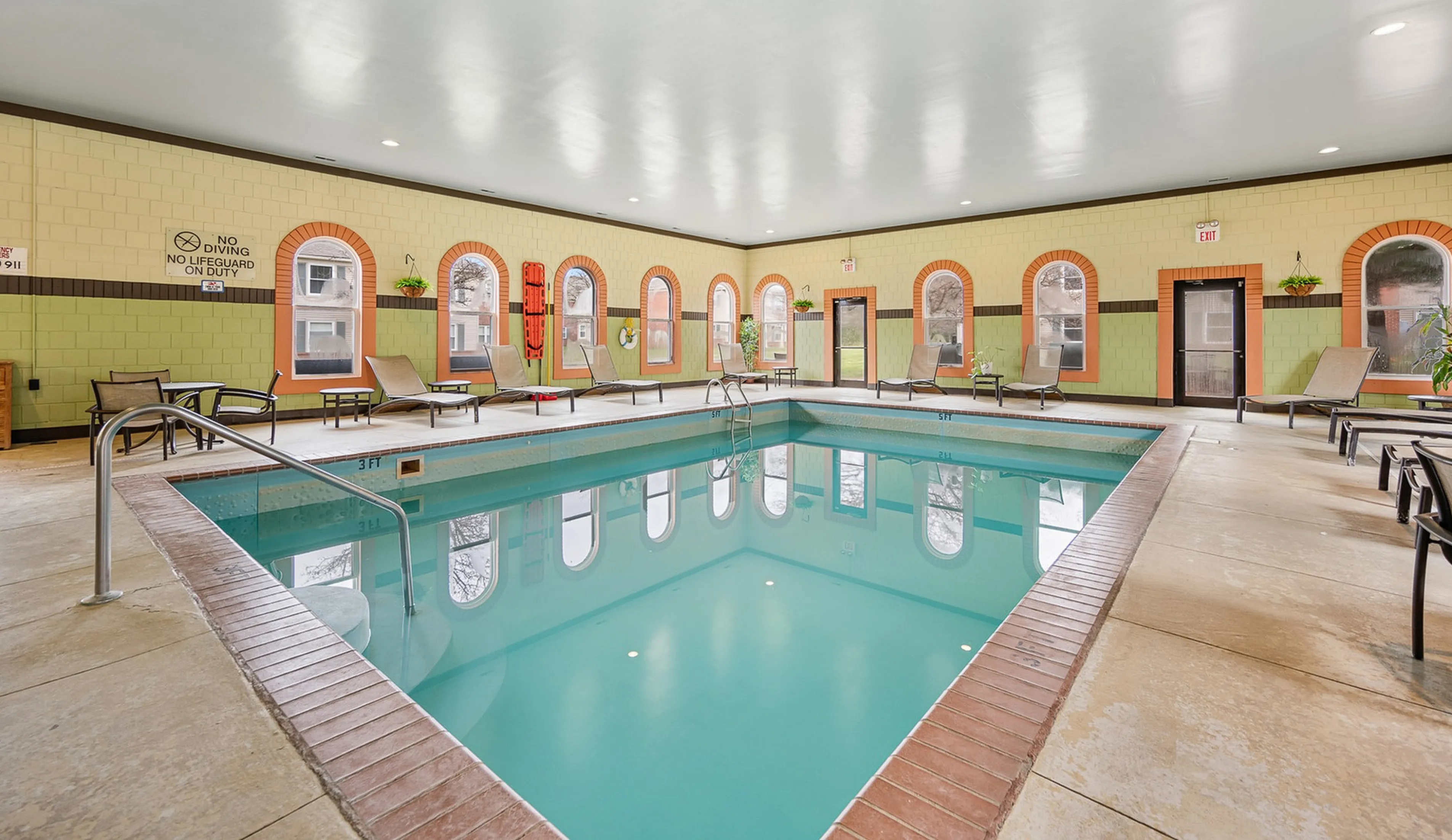 Inviting indoor pool area with relaxing lounge chairs, natural light from arched windows, and vibrant decor.