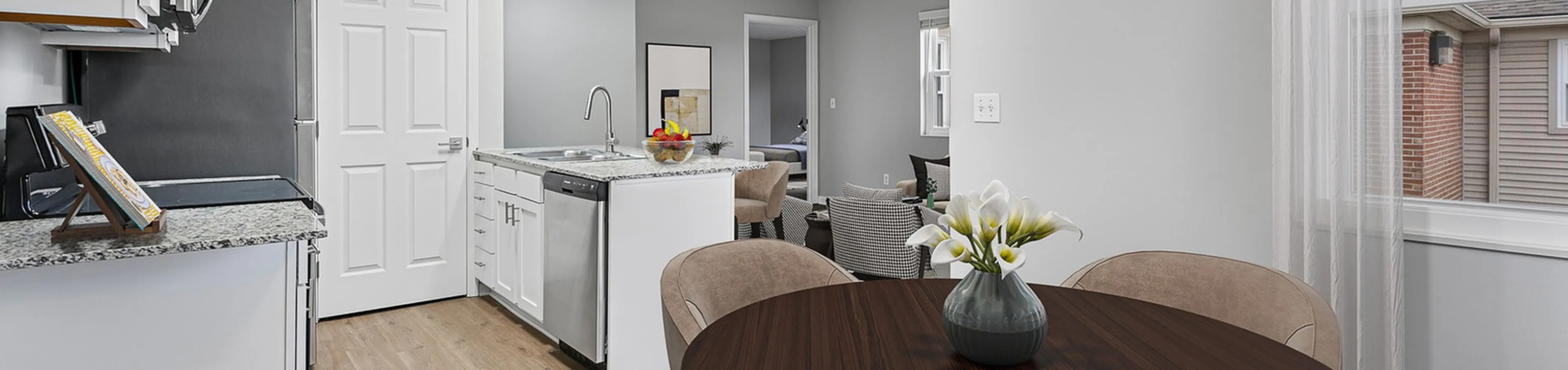 Bright and modern open-concept kitchen and dining area with stylish granite countertops, sleek stainless steel appliances, and elegant wooden dining table.
