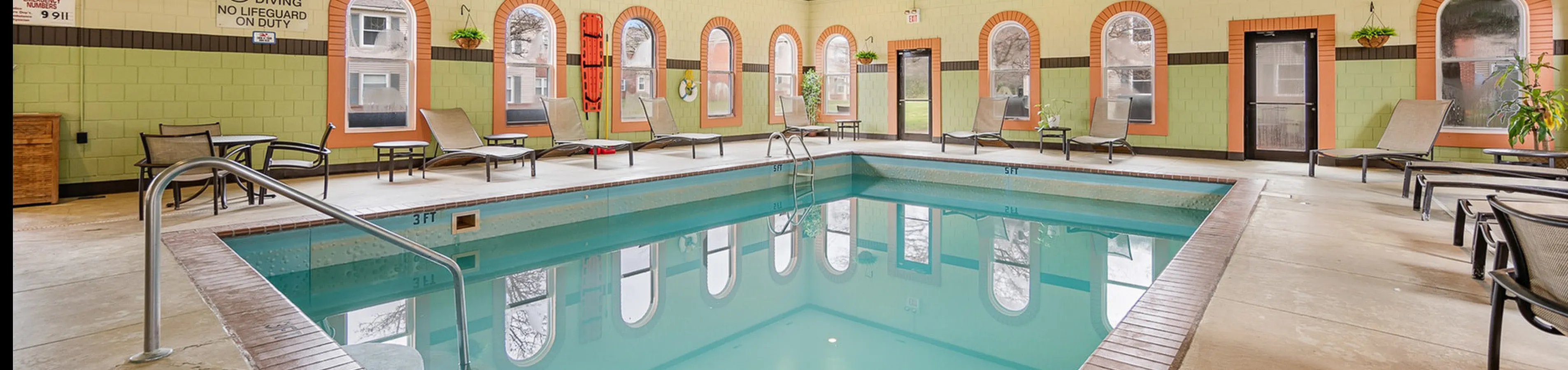 Inviting indoor swimming pool area with stylish lounge chairs and vibrant wall accents, perfect for relaxation and leisure.