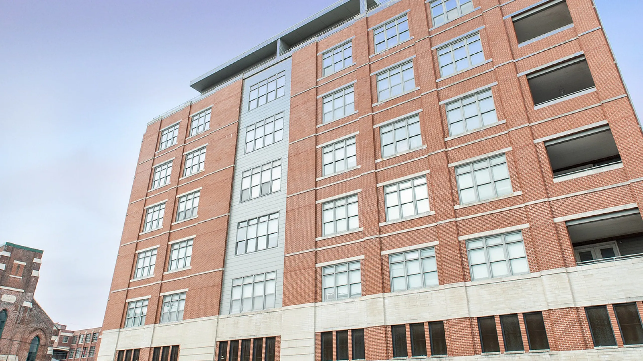 Modern brick apartment building with large windows against a clear blue sky, showcasing urban elegance and contemporary design.