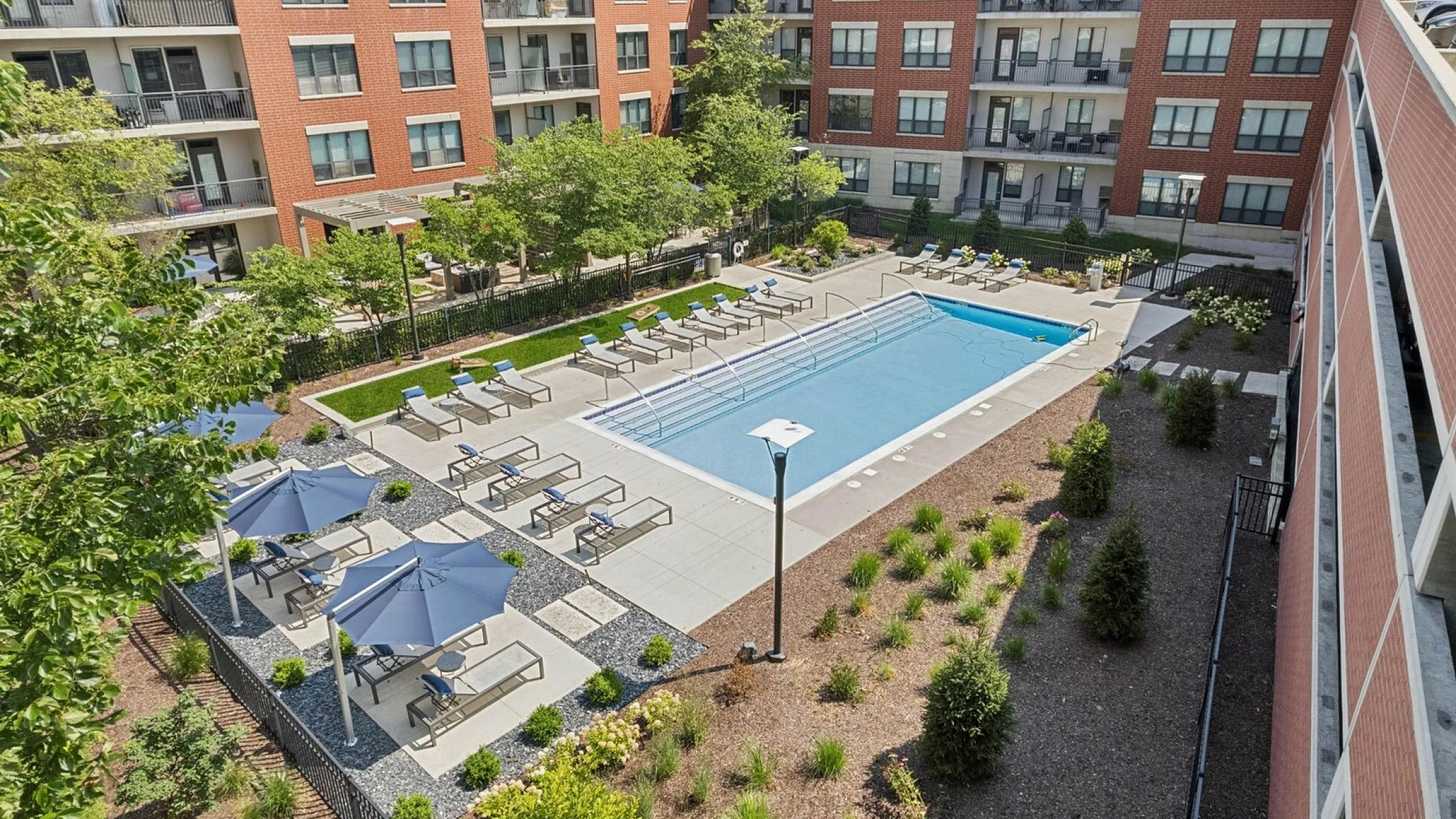 Luxurious apartment complex courtyard featuring a sparkling swimming pool, surrounded by elegant sun loungers and landscaped greenery.