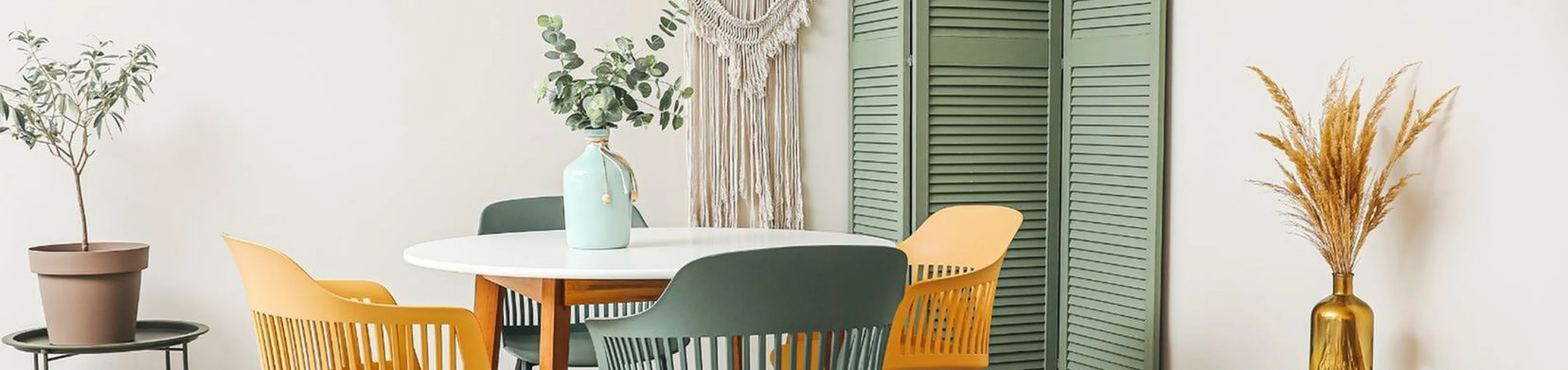 Chic dining area with a modern round table, stylish mixed-color chairs, and elegant decor including abstract art and lush greenery.