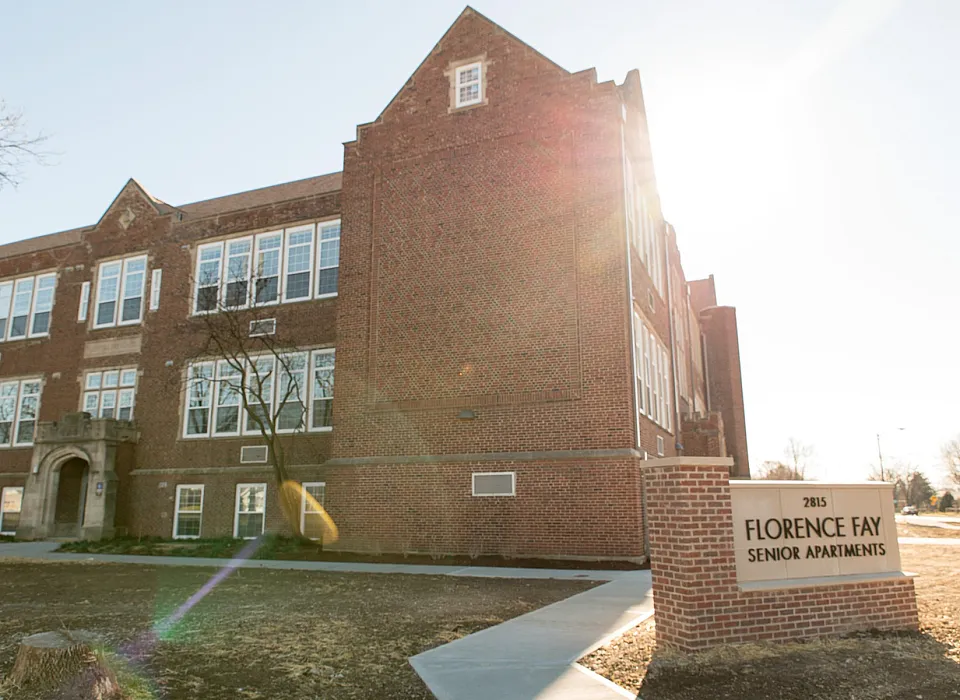 Charming red-brick senior apartment building with large windows and elegant architectural design, surrounded by a peaceful, sunlit neighborhood.