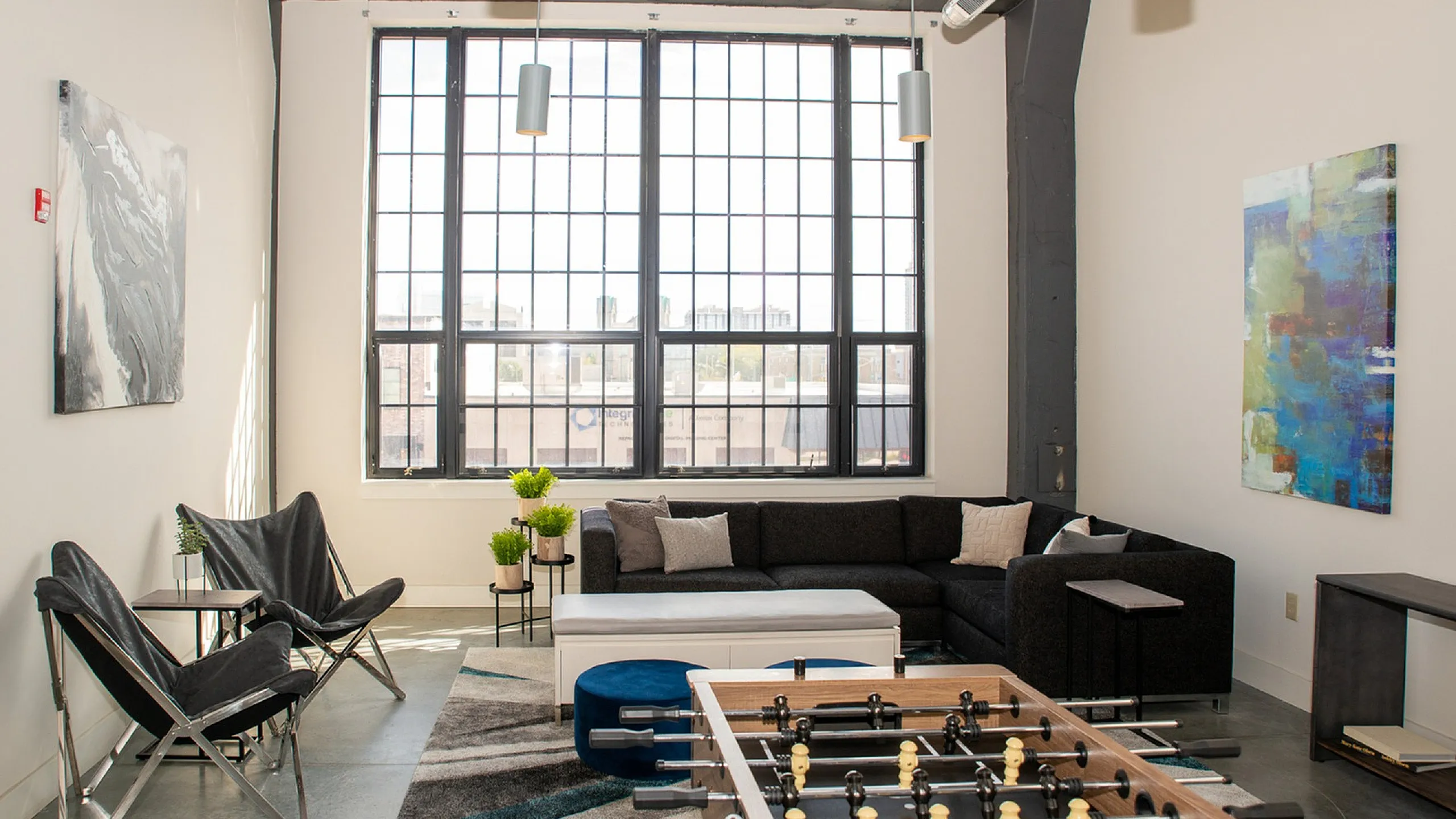 Bright and modern living space with large industrial windows, stylish decor, and a fun foosball table, ideal for entertaining.
