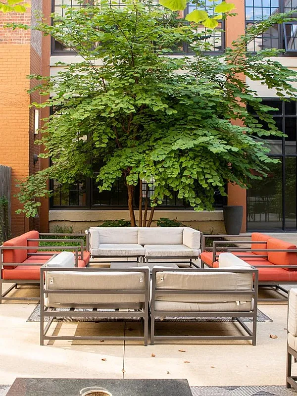 Charming courtyard with stylish outdoor seating, lush greenery, and vibrant brick building backdrop, ideal for relaxation and social gatherings.