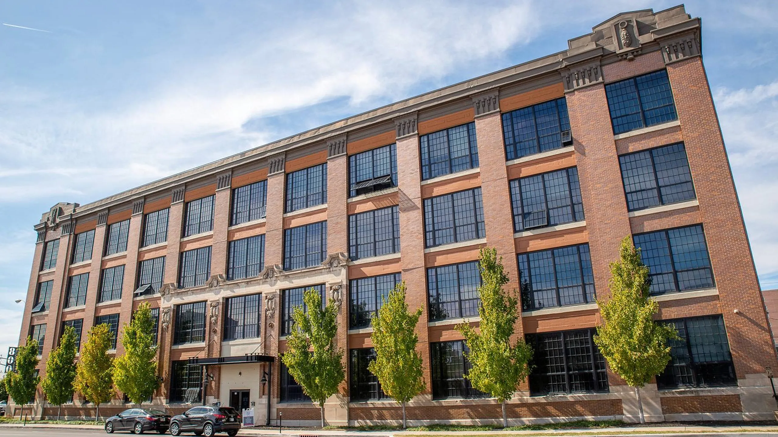Beautifully restored historic brick building with large windows and tree-lined facade, offering versatile loft-style apartments.