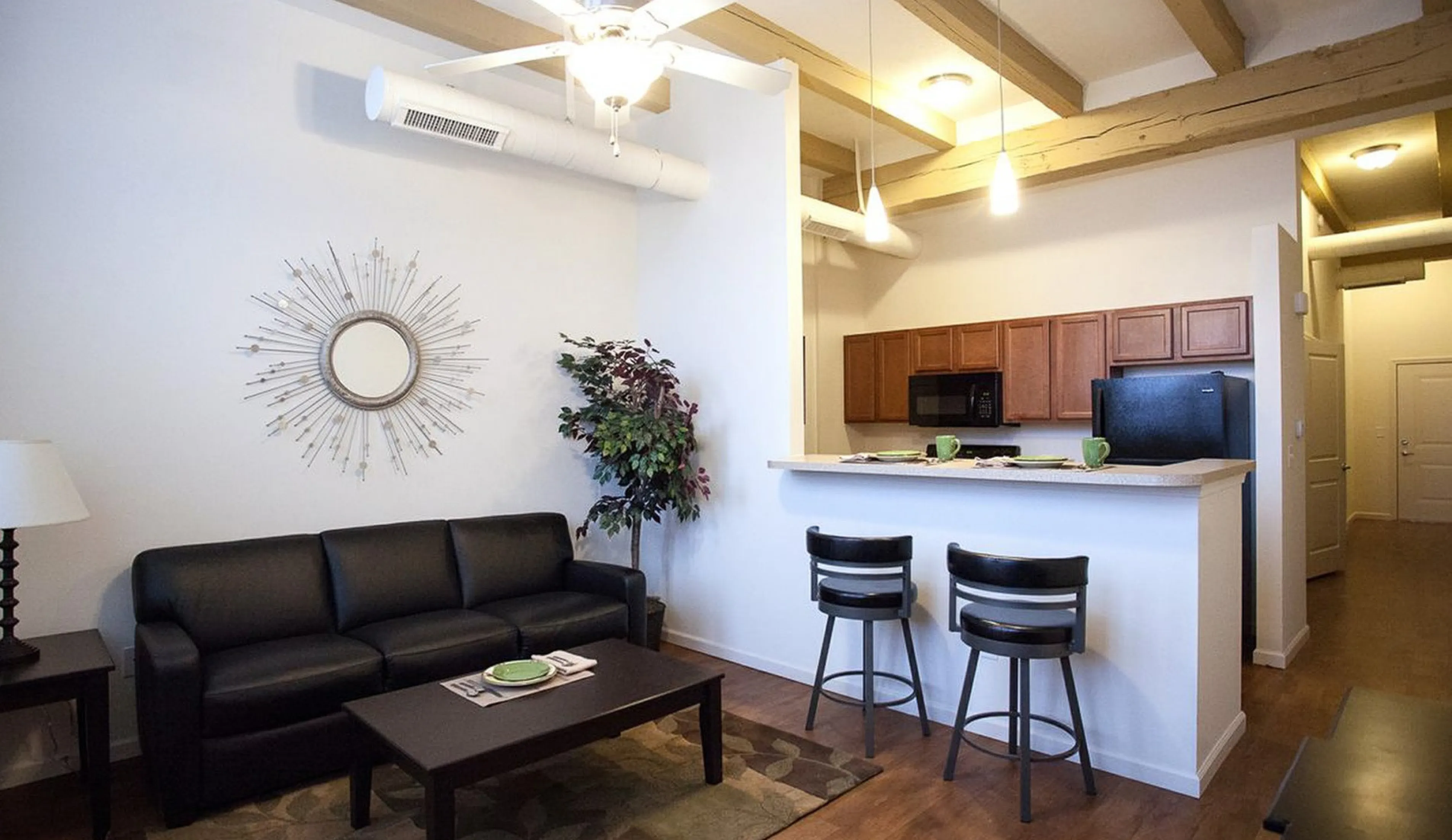 Modern apartment living room with sleek leather sofa, stylish wall decor, and open kitchen area with bar seating.
