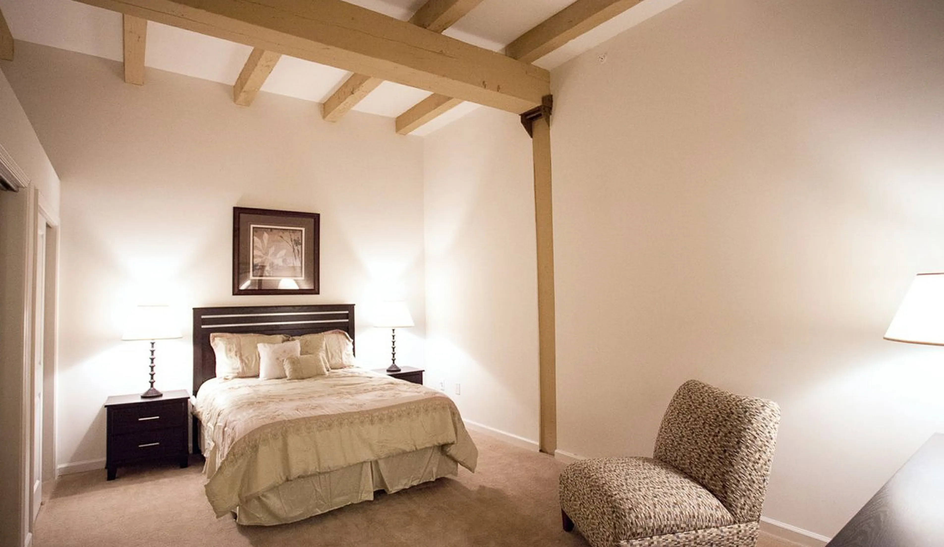 Cozy bedroom with elegant wooden beams, featuring a plush bed, stylish nightstands, and a chic accent chair, creating a warm and inviting atmosphere.