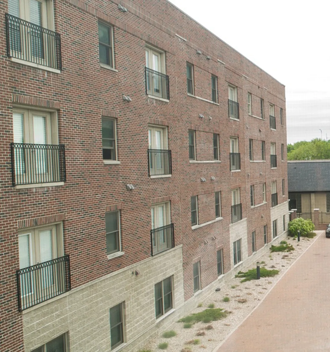 Charming brick apartment building with ample parking, nestled in a vibrant neighborhood with lush greenery and convenient road access.