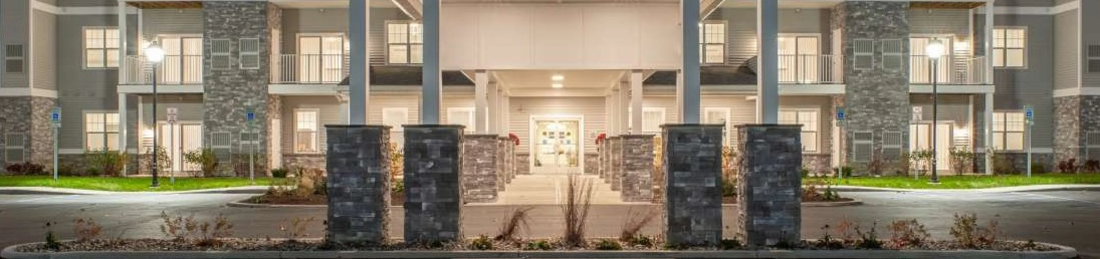 Elegant apartment complex with modern architecture, featuring well-lit balconies and a grand entrance at dusk.