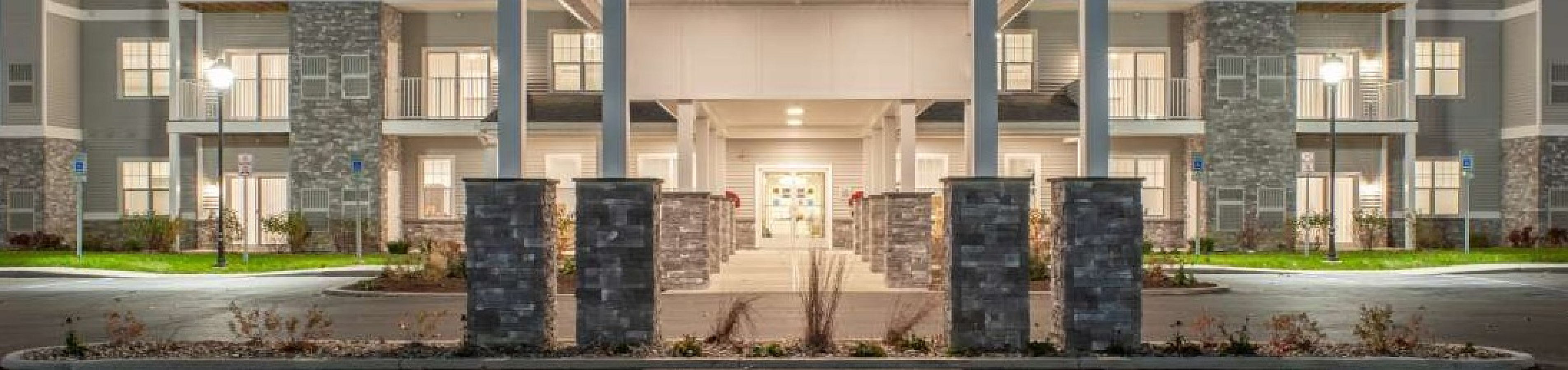 Elegant apartment complex with modern architecture, featuring well-lit balconies and a grand entrance at dusk.