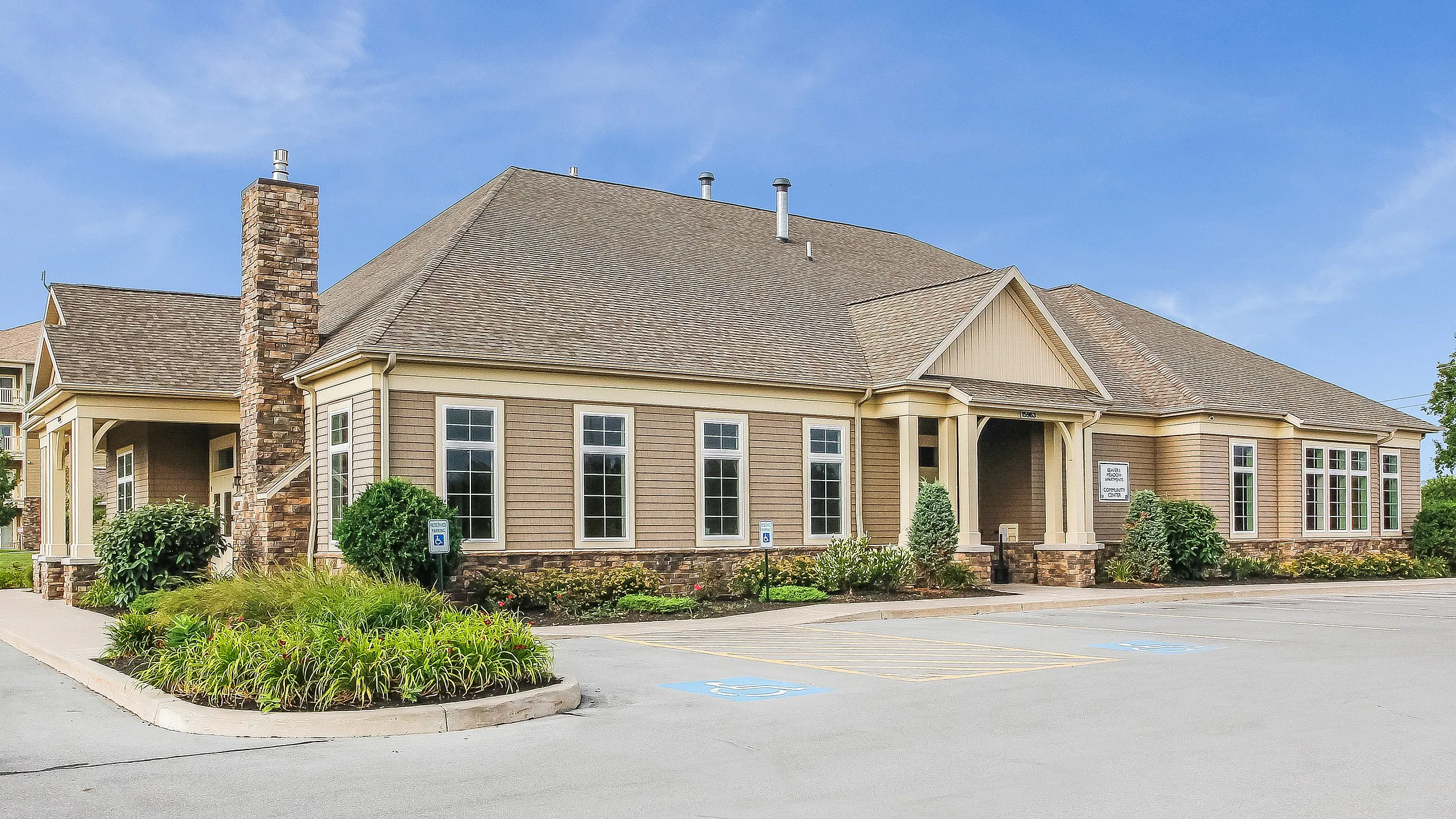 Charming community center with rustic architectural design, surrounded by manicured greenery and ample parking space.