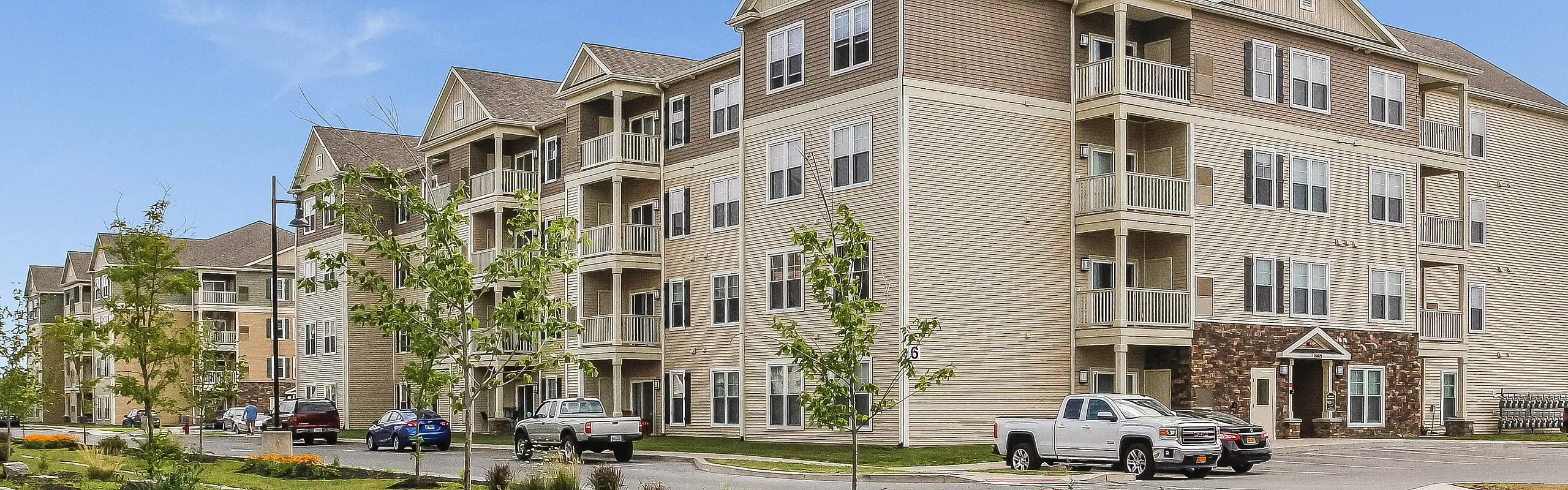 Charming four-story apartment complex with stylish balconies, surrounded by lush landscaping and ample parking, under a clear blue sky.