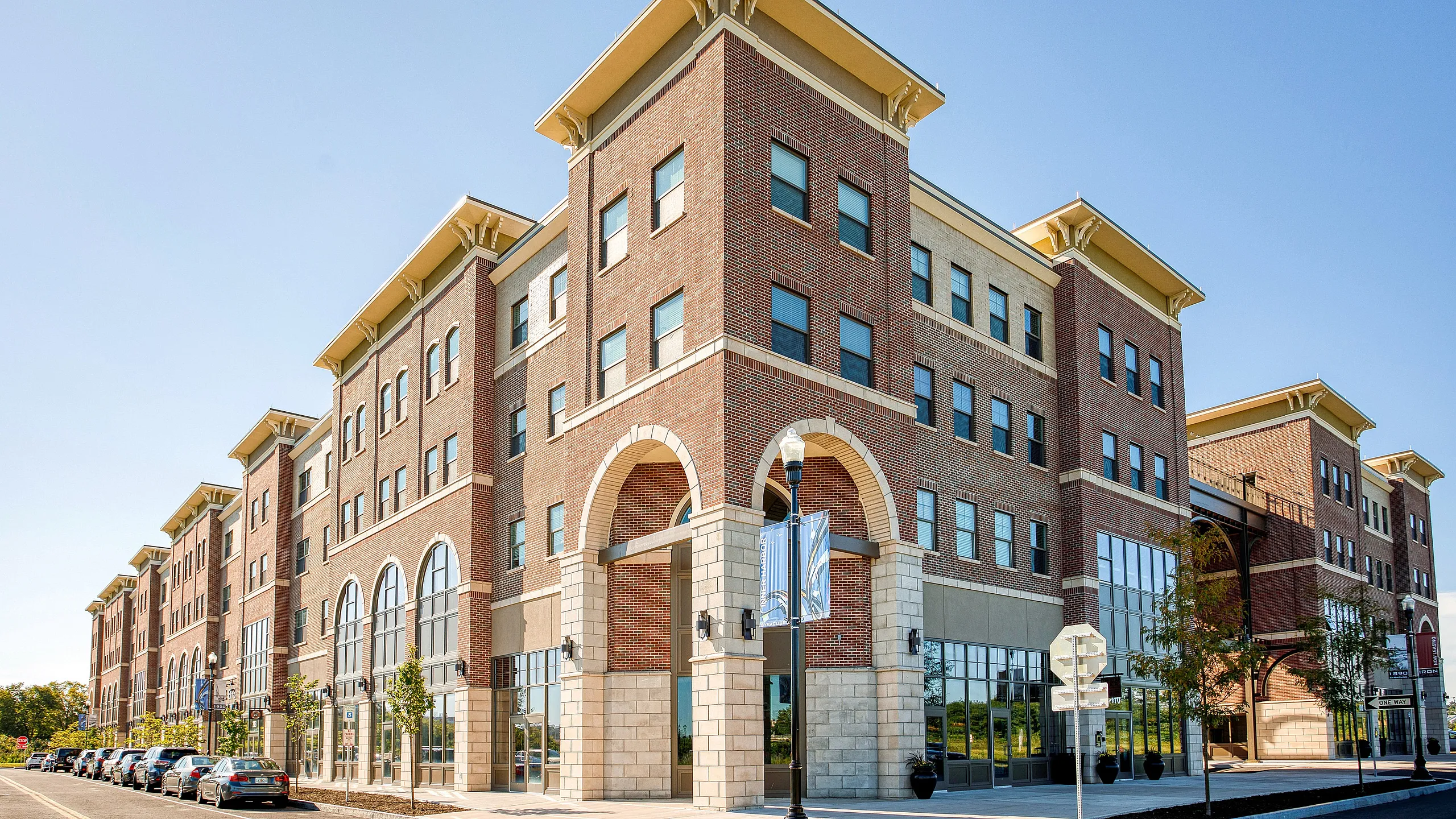 Elegant brick building with modern design, featuring large arched windows and vibrant storefronts, set against a clear blue sky.