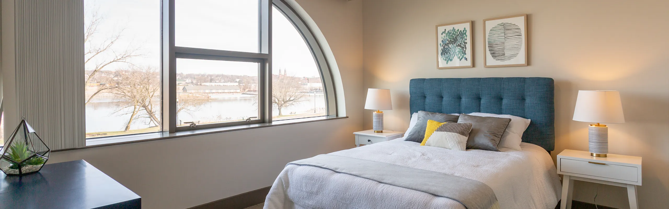 Bright and stylish bedroom with scenic river view, featuring a plush blue headboard, cozy bedding, and chic decor.