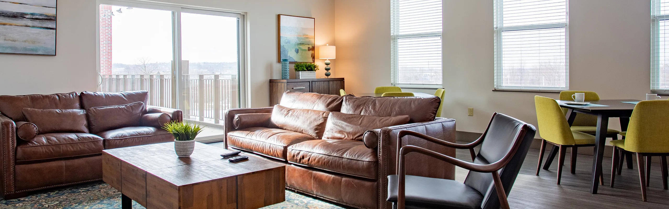Bright, modern living room featuring plush leather sofas, a chic wooden coffee table, and a stylish open-concept dining area with vibrant green chairs.