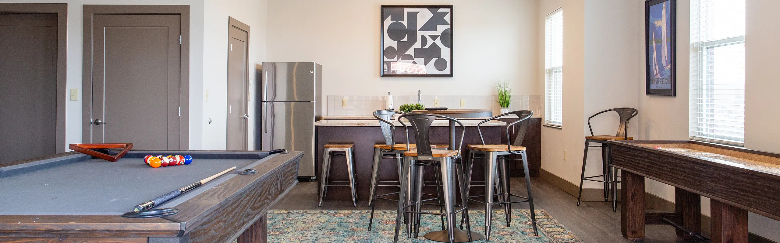 Chic recreation room featuring a luxurious pool table, stylish bar seating, and natural light pouring in for a lively atmosphere.