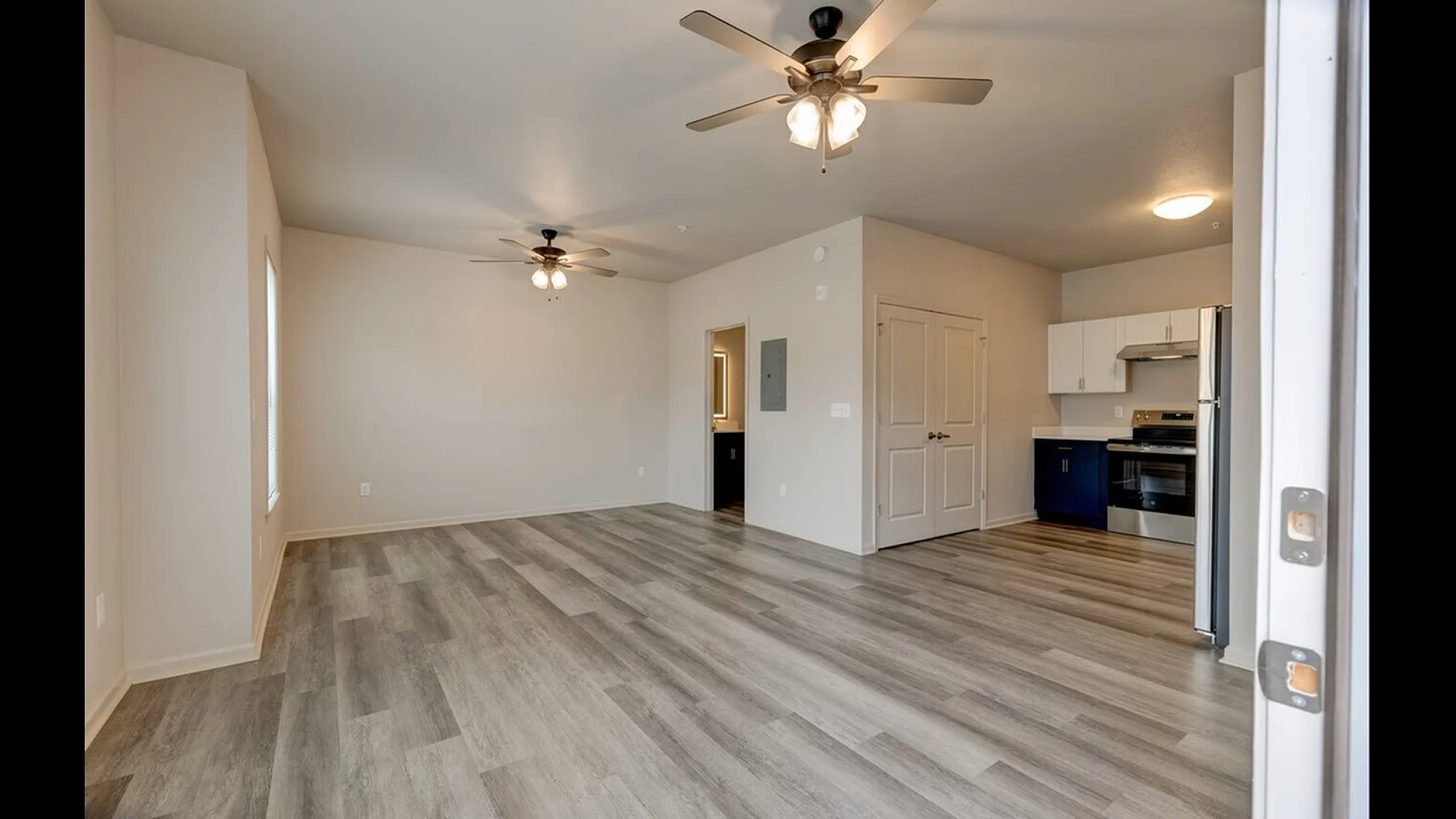 Modern open-concept apartment with stylish wood flooring, ceiling fans, and a sleek kitchen featuring stainless steel appliances.