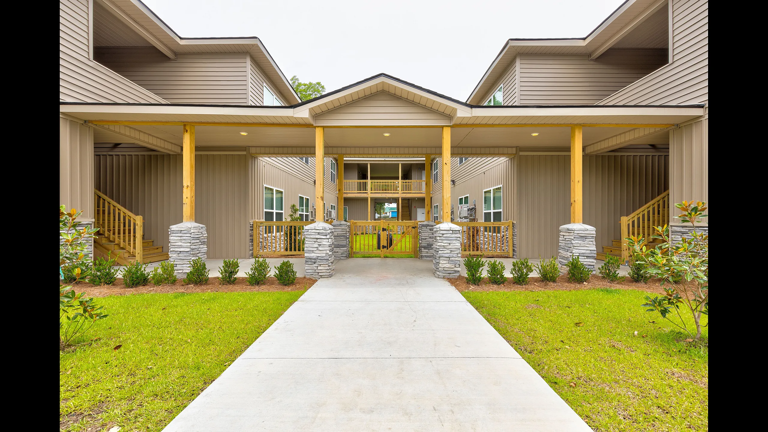 Charming modern apartment complex with stylish wooden features, lush greenery, and inviting entryway.