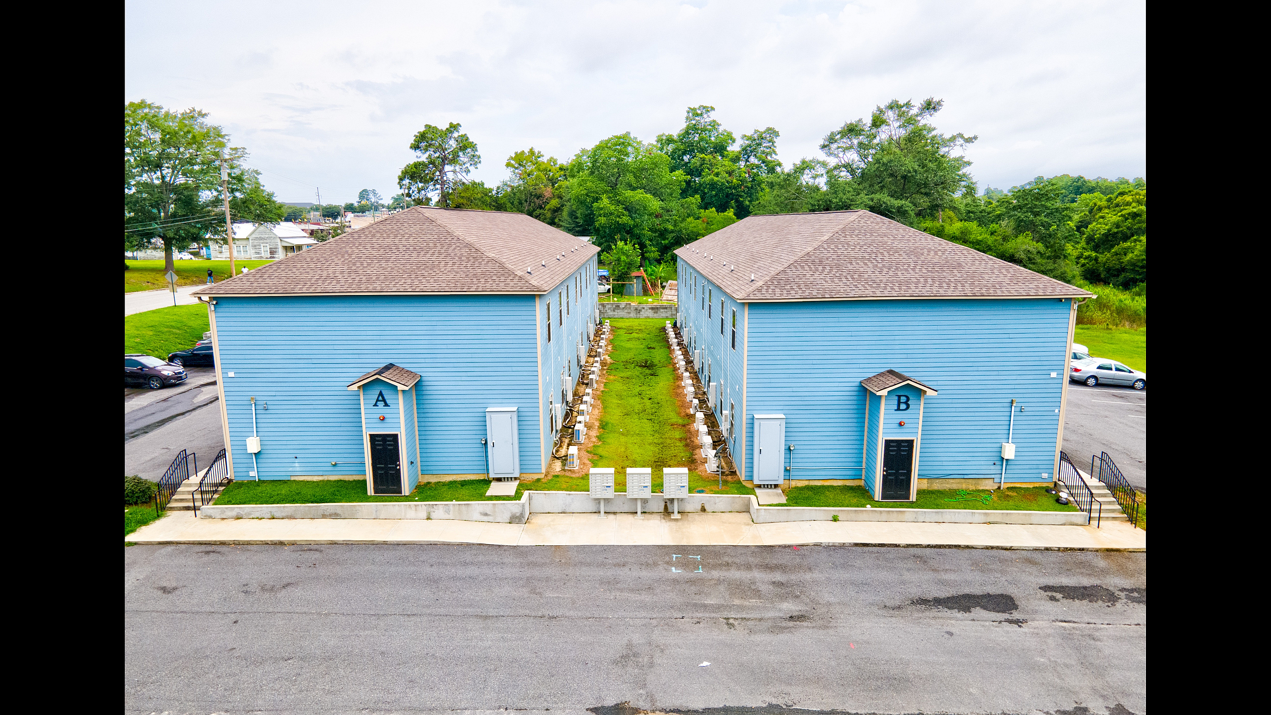 Charming blue duplexes with ample parking, lush green surroundings, and a peaceful neighborhood vibe.
