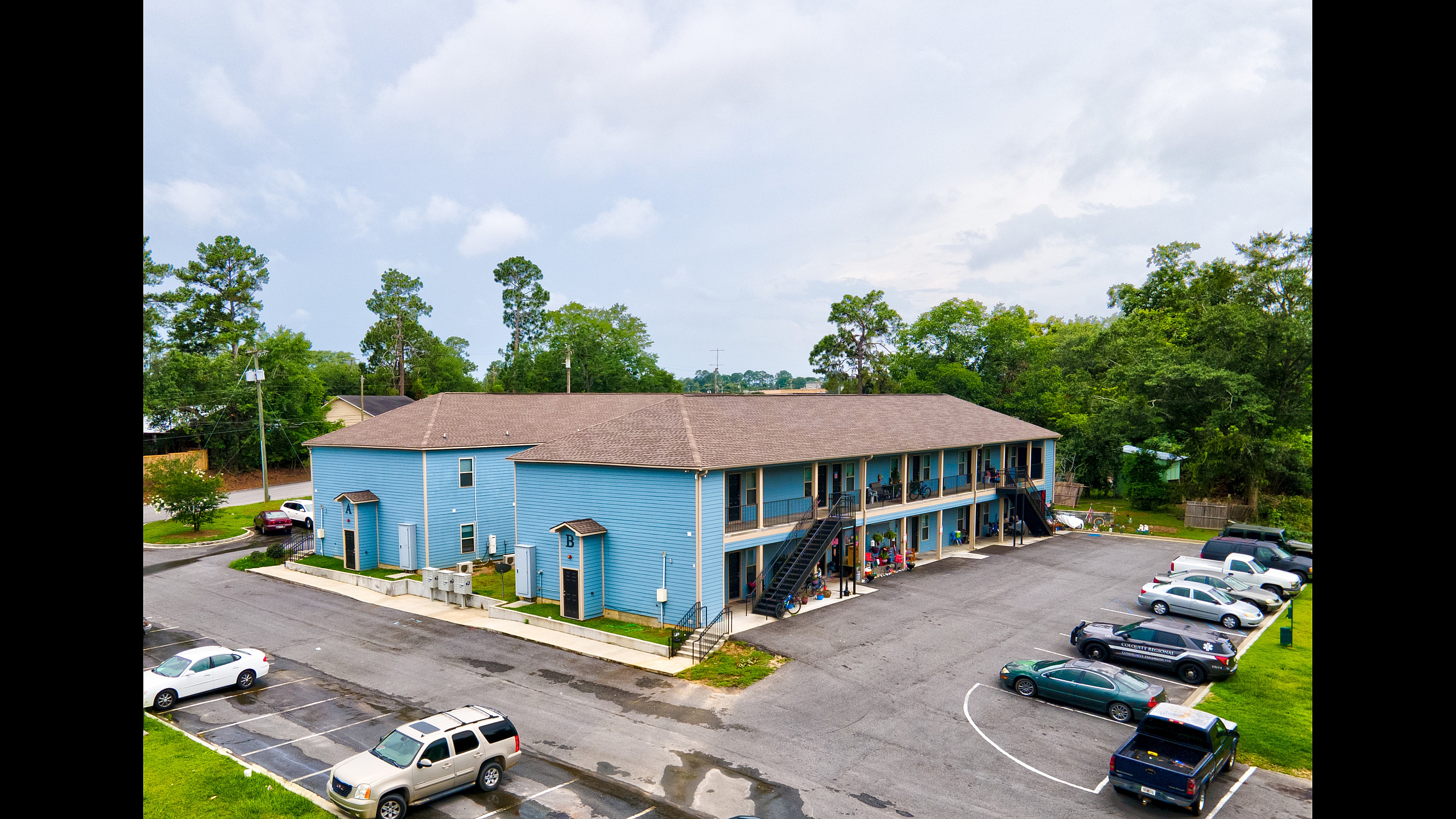 Vibrant blue apartment complex with a spacious parking lot and lush green surroundings offering convenient urban living.
