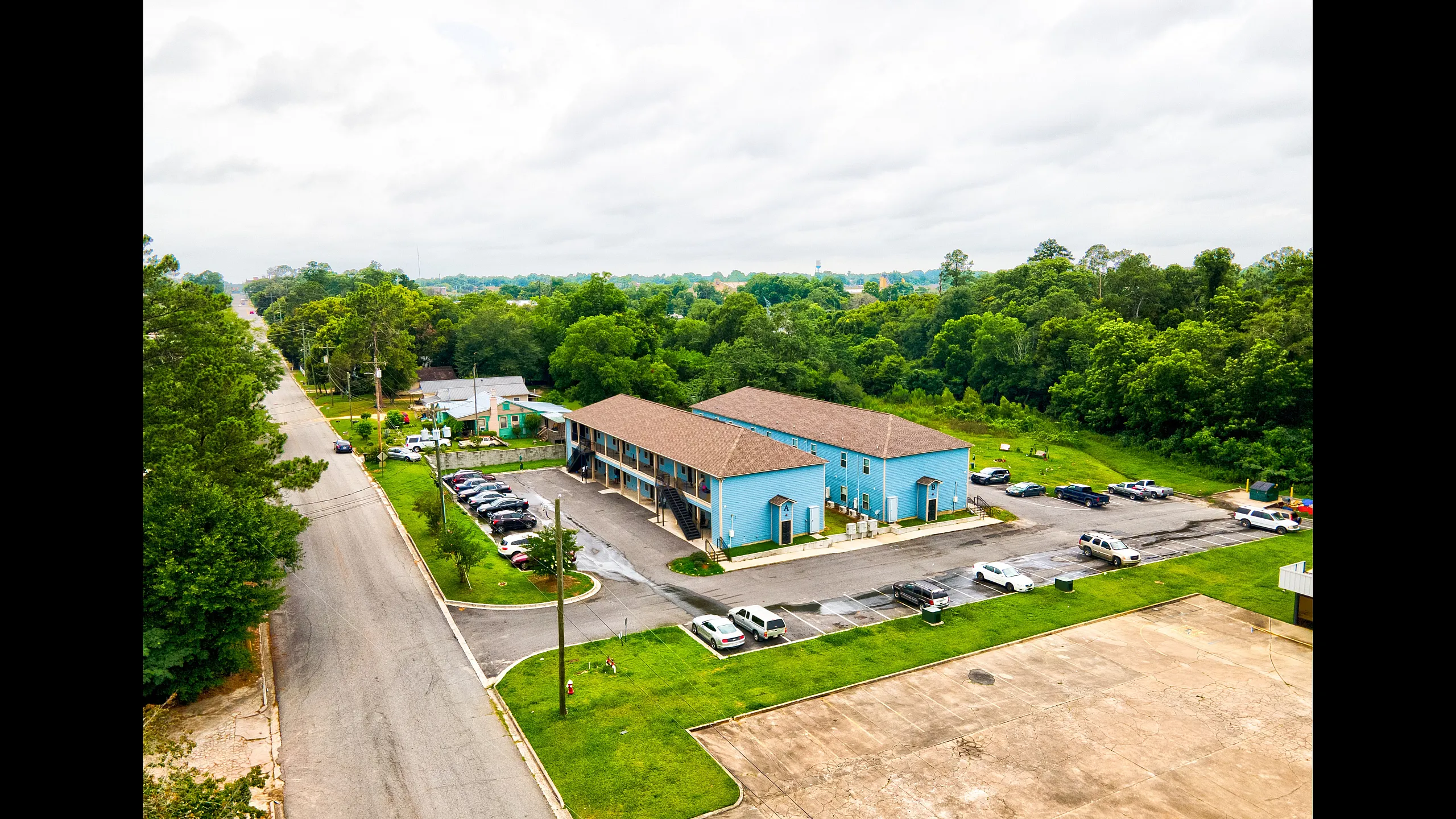 Charming two-story blue apartment complex surrounded by lush greenery, offering convenient parking and a peaceful suburban setting.