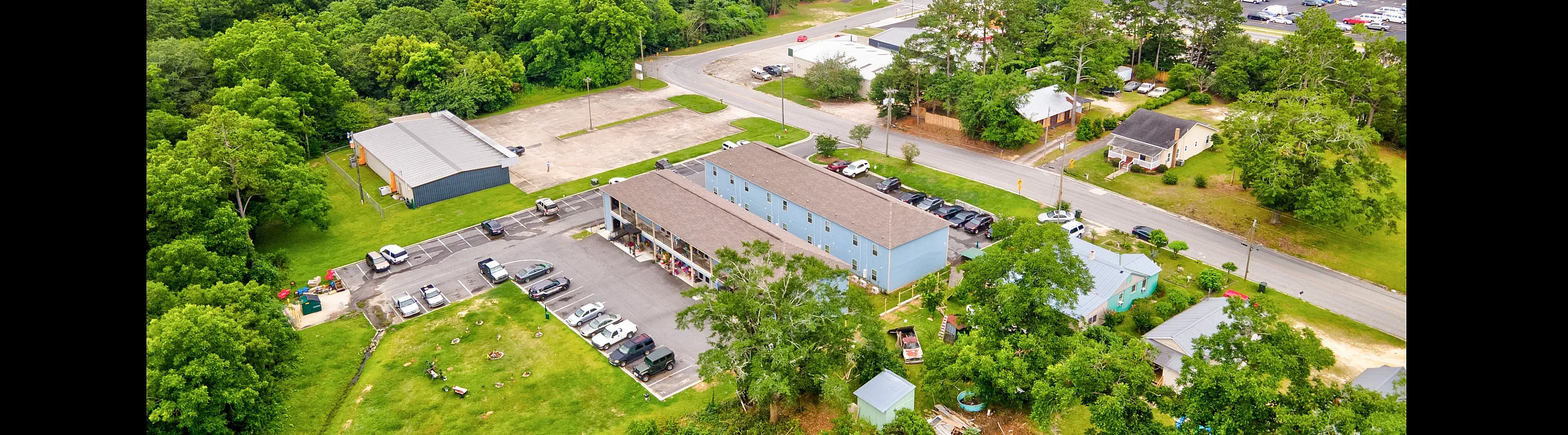 Vibrant aerial view of a charming apartment complex surrounded by lush greenery and a bustling neighborhood, showcasing ample parking and proximity to amenities.