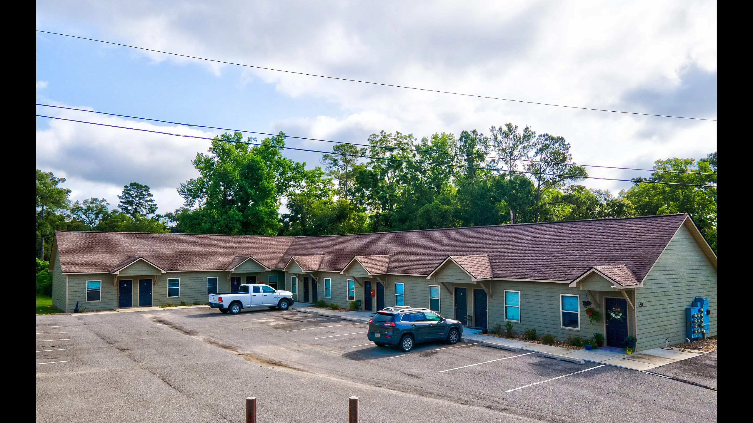 Charming row of connected cottages with inviting exteriors, surrounded by lush greenery, offering ample parking and a serene atmosphere.