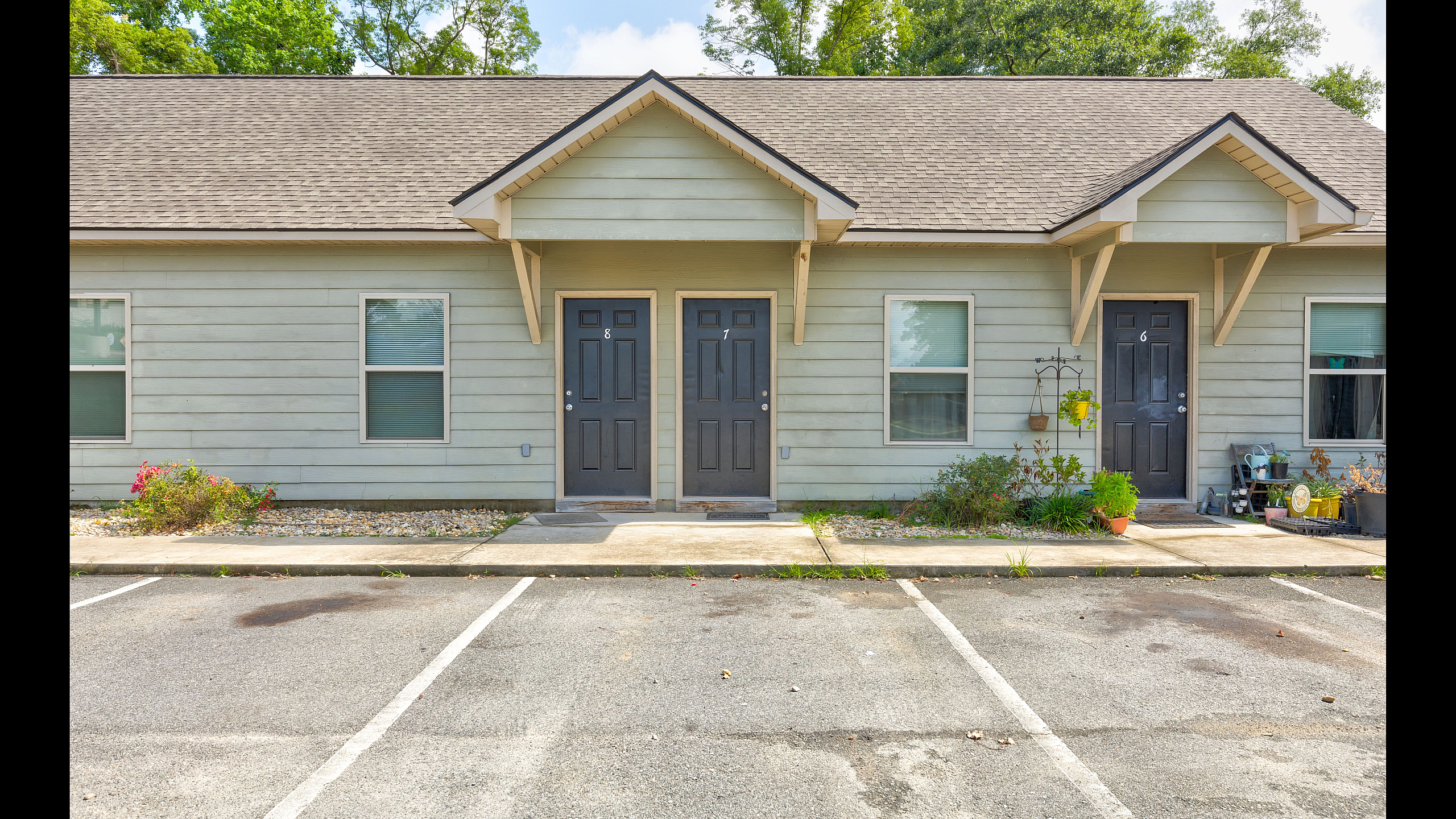 Charming townhouse exterior featuring three elegant entrances, vibrant greenery, and convenient parking spaces.