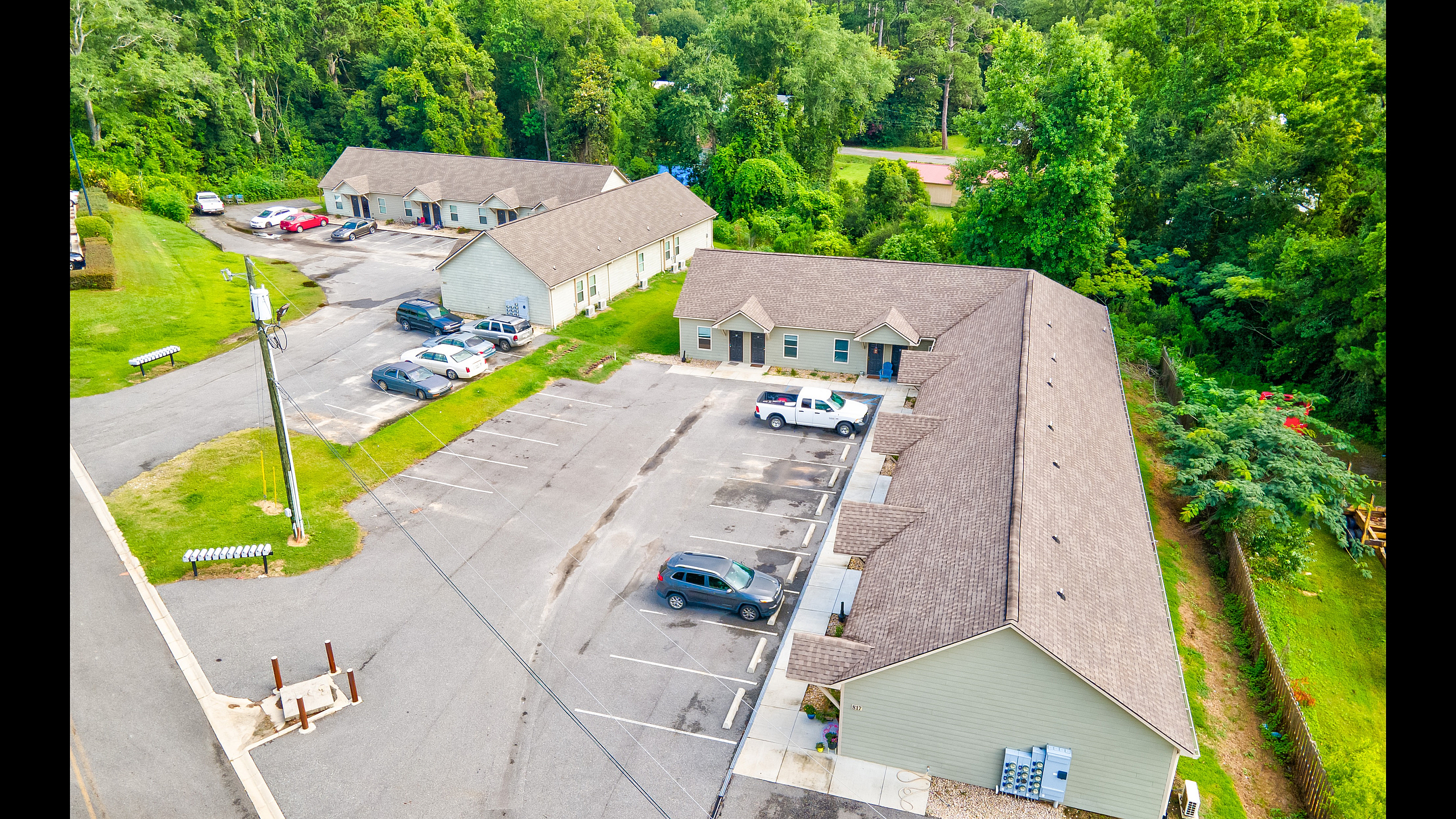 Aerial view of charming apartment complex surrounded by lush greenery, featuring ample parking and a serene suburban setting.