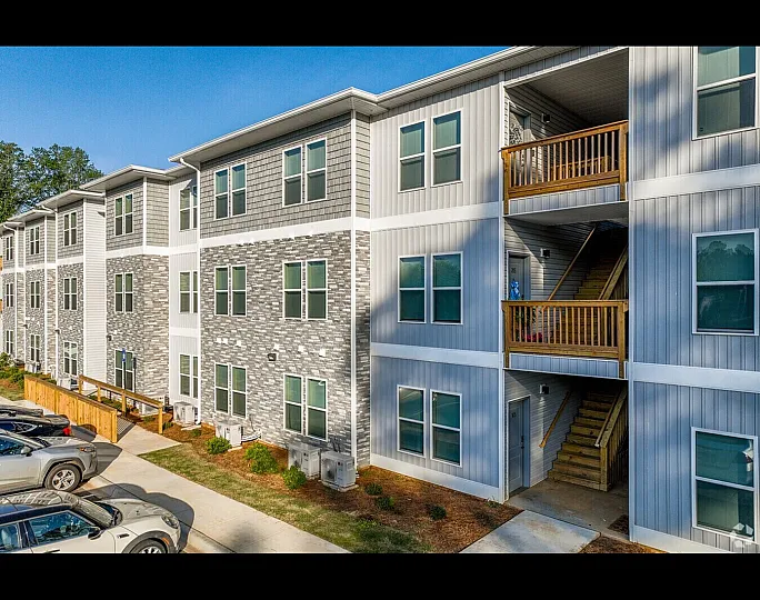 Modern three-story apartment building with attractive brick and siding facade, featuring spacious balconies and convenient parking area.