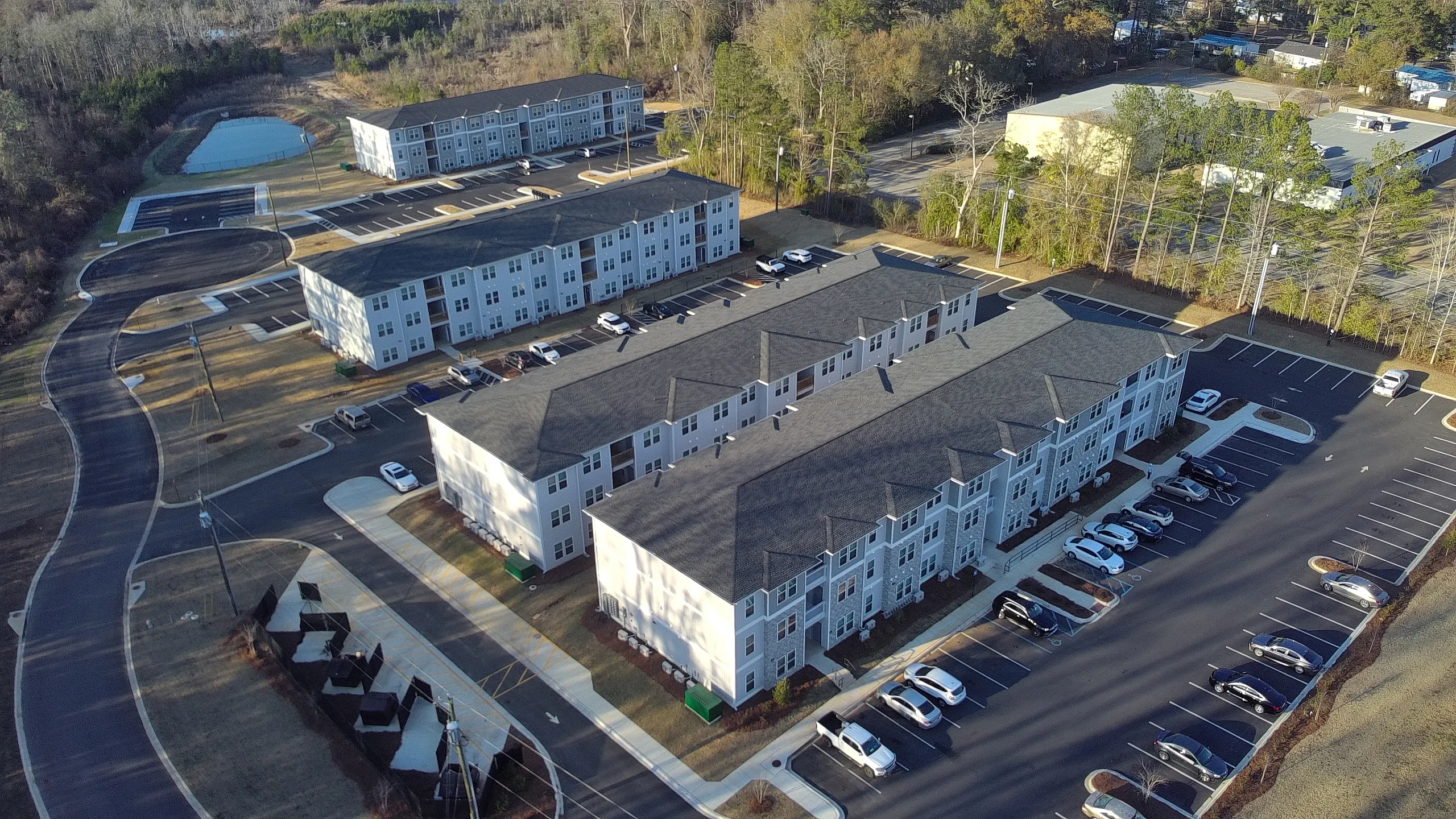 Aerial view of modern, serene apartment complex surrounded by lush greenery, featuring ample parking and scenic pathways.