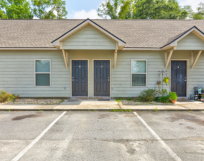 Charming duplex exterior with stylish gray doors and landscaped front with blooming plants, promising cozy living.