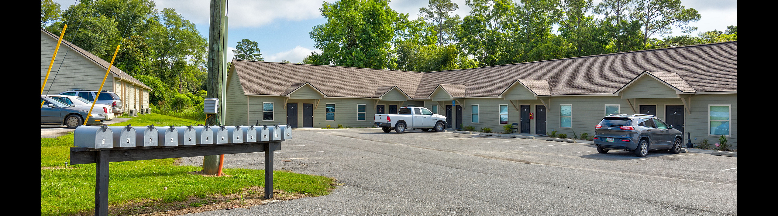 Charming apartment complex with well-maintained exteriors, ample parking, and a row of mailboxes, nestled in a lush green setting.