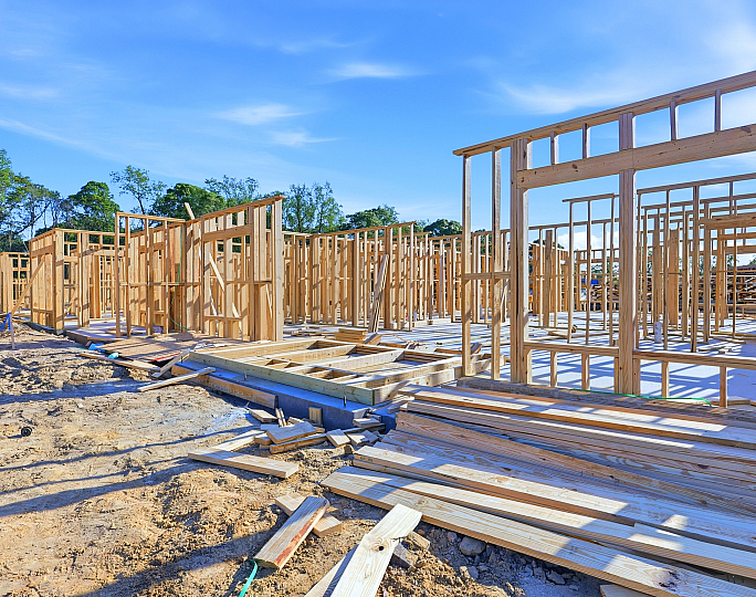 Bright construction site with a promising framework for spacious modern homes, set against a clear blue sky.