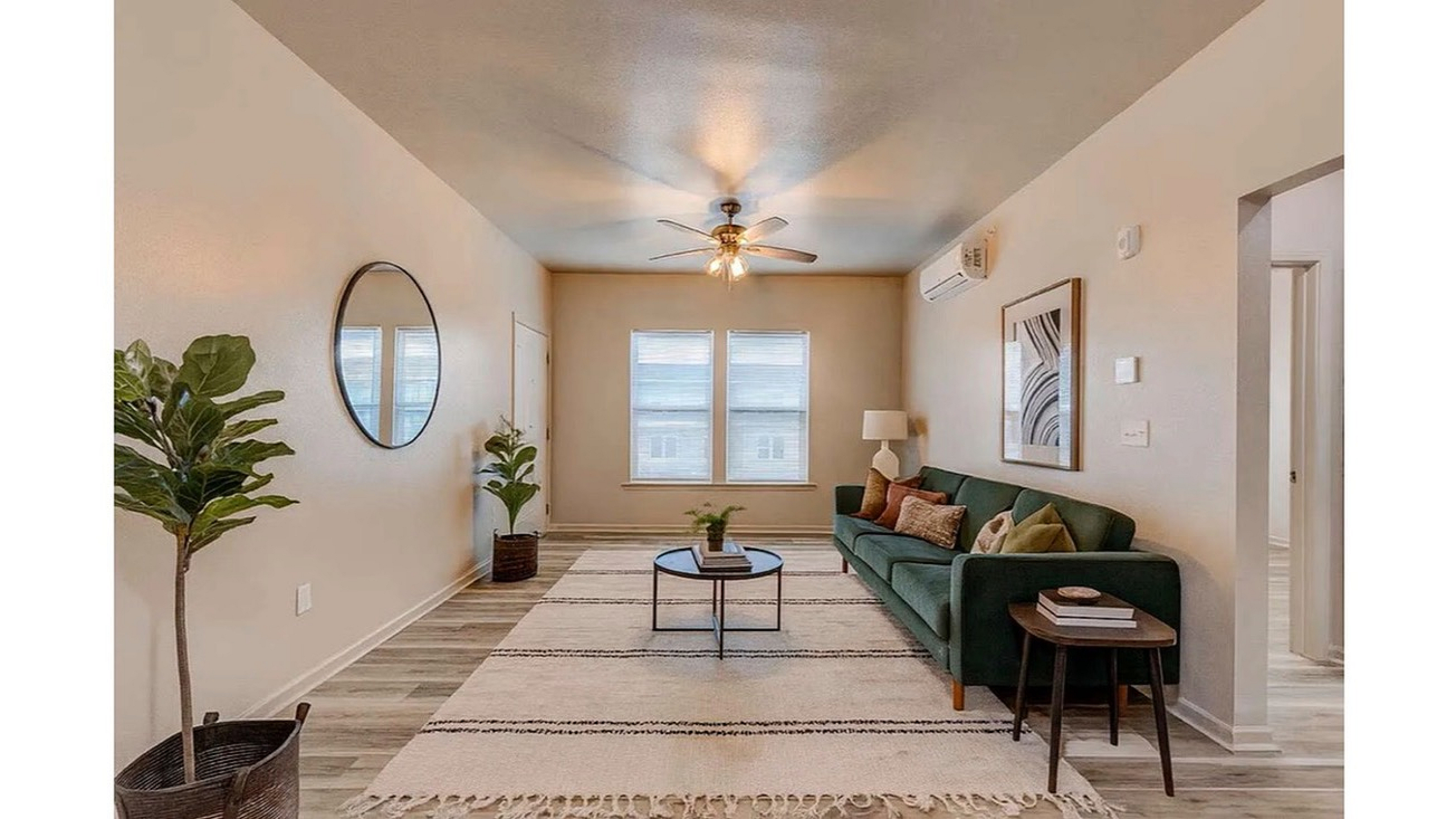 Chic living room with modern decor, featuring a plush green sofa, stylish mirror, and elegant ceiling fan, bathed in natural light.