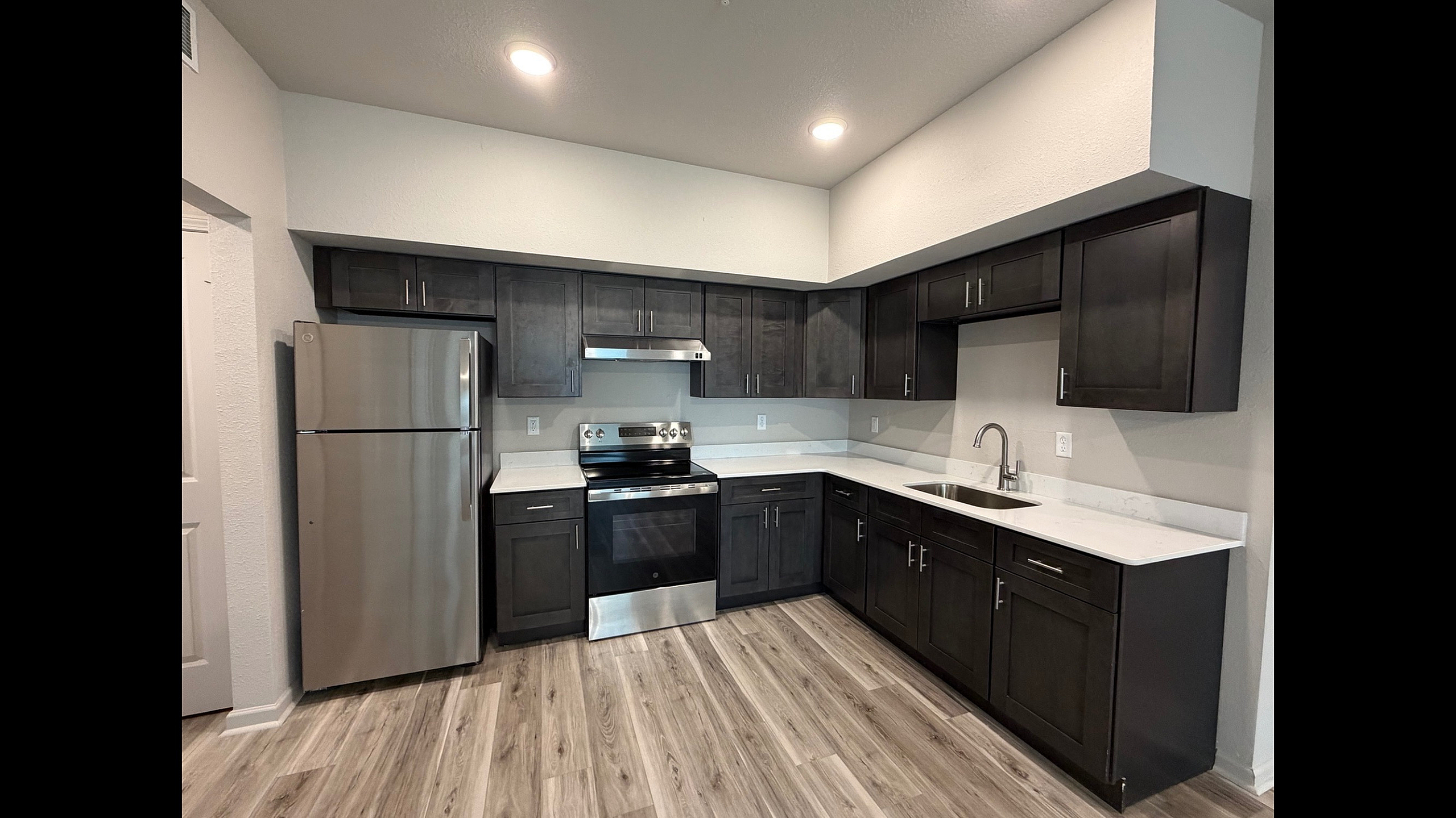 Modern kitchen with sleek dark wood cabinets, stainless steel appliances, and elegant wood flooring.