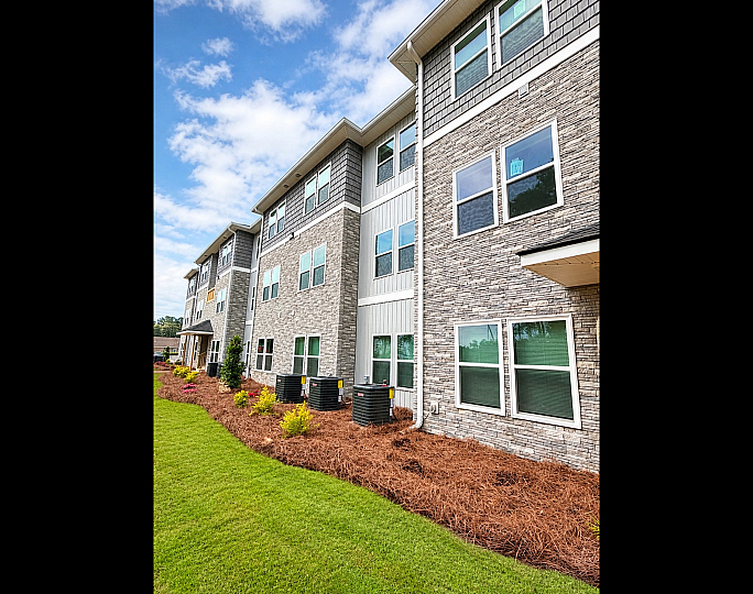 Modern apartment building with elegant stone facade, lush landscaping, and large windows under a bright blue sky.