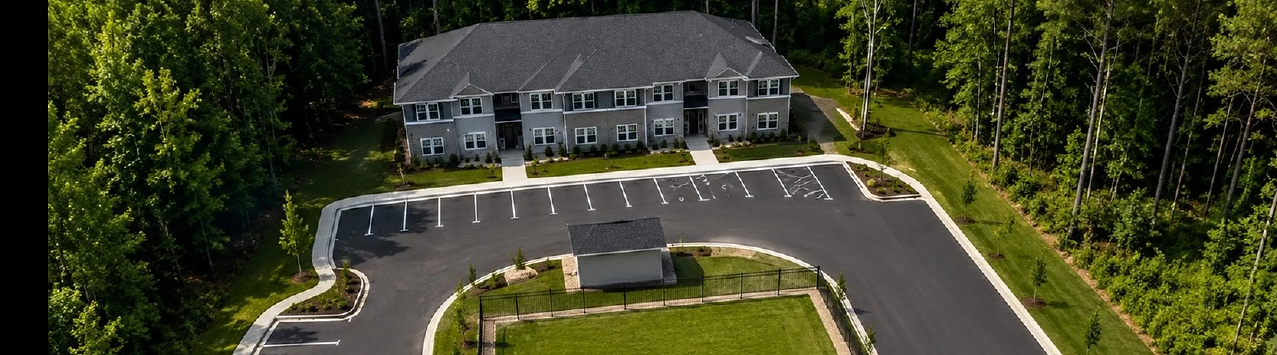 Aerial view of a modern apartment complex surrounded by lush greenery, featuring ample parking space and beautifully landscaped grounds.