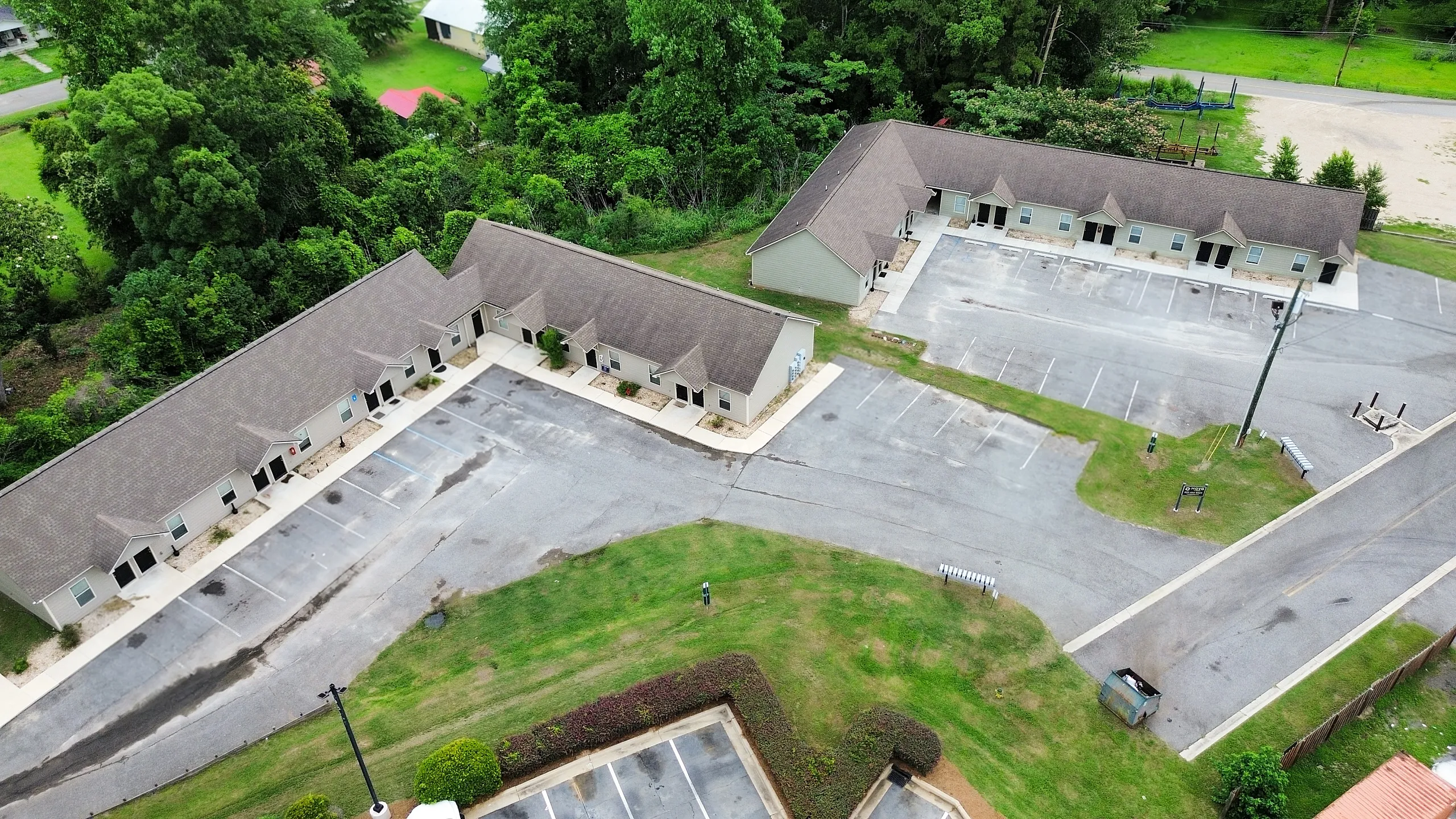 Aerial view of charming townhouses surrounded by lush greenery, featuring ample parking and a serene environment.