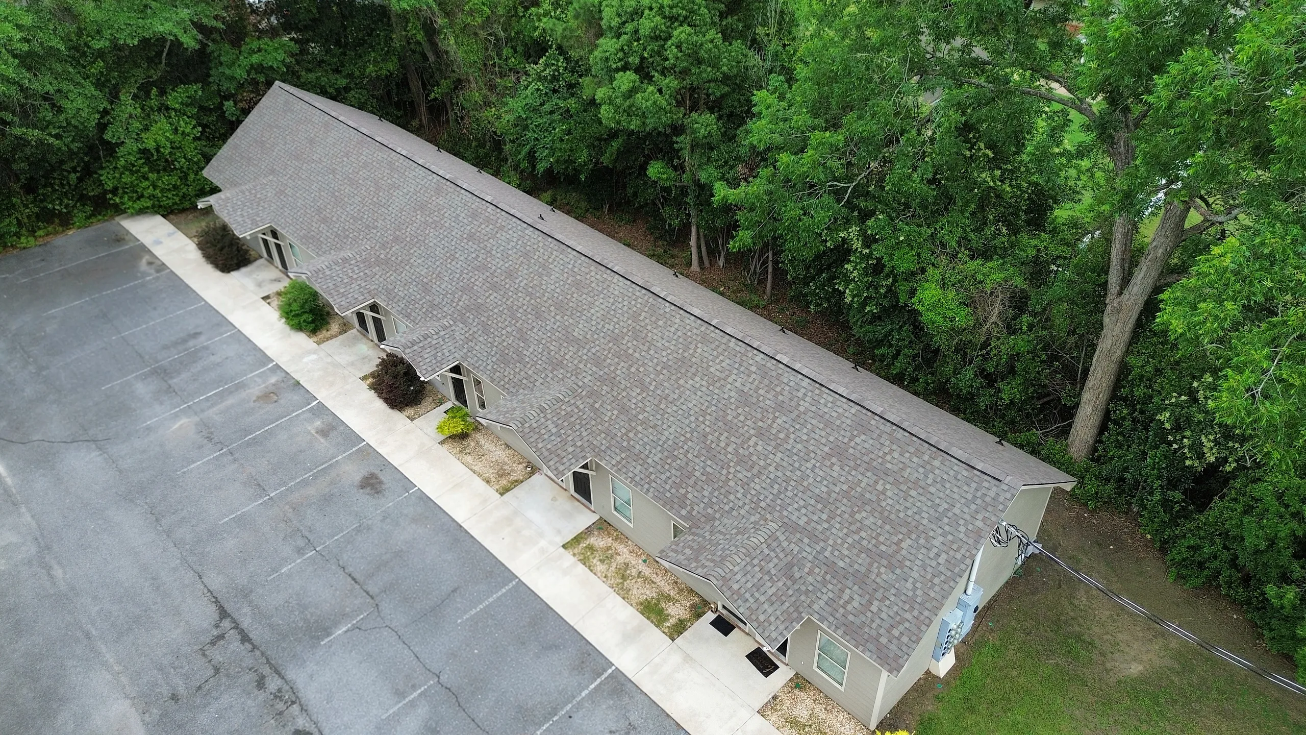 Aerial view of a charming apartment complex nestled among lush greenery, featuring ample parking and a modern design.