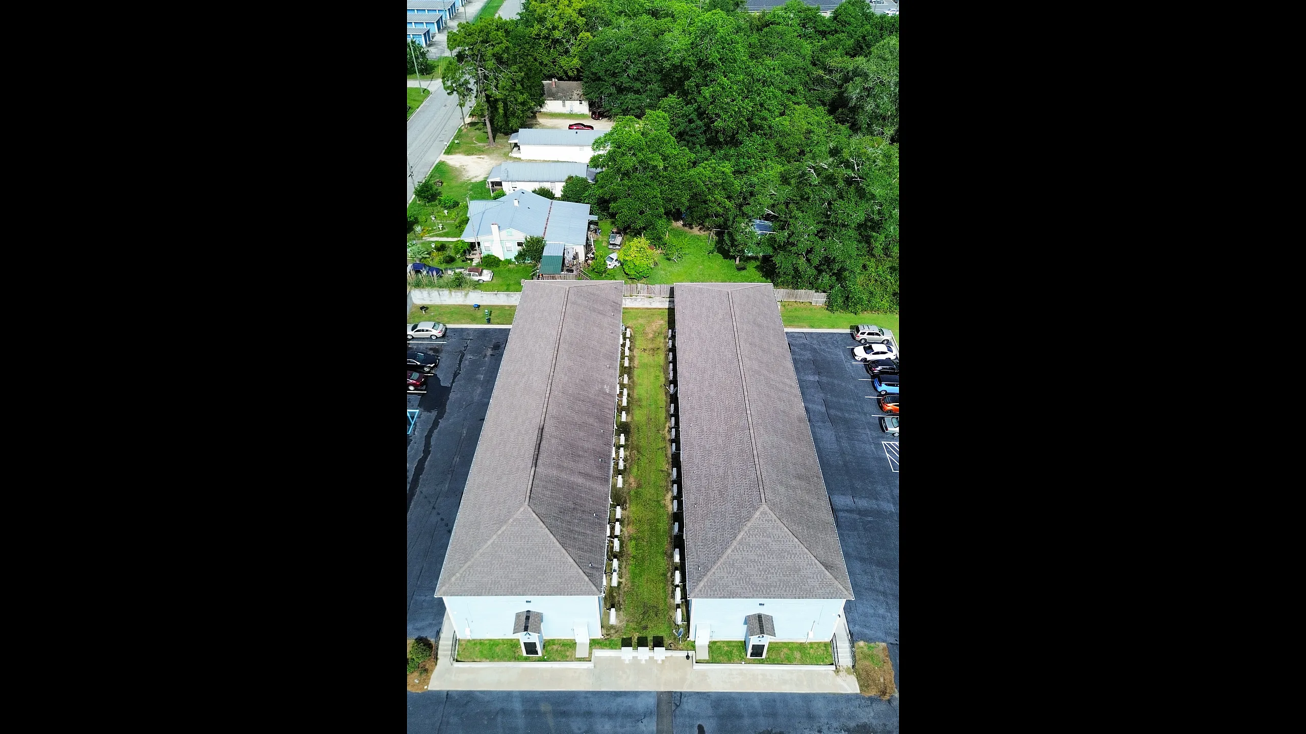 Aerial view of a charming apartment complex with two parallel buildings, lush green surroundings, and ample parking space.