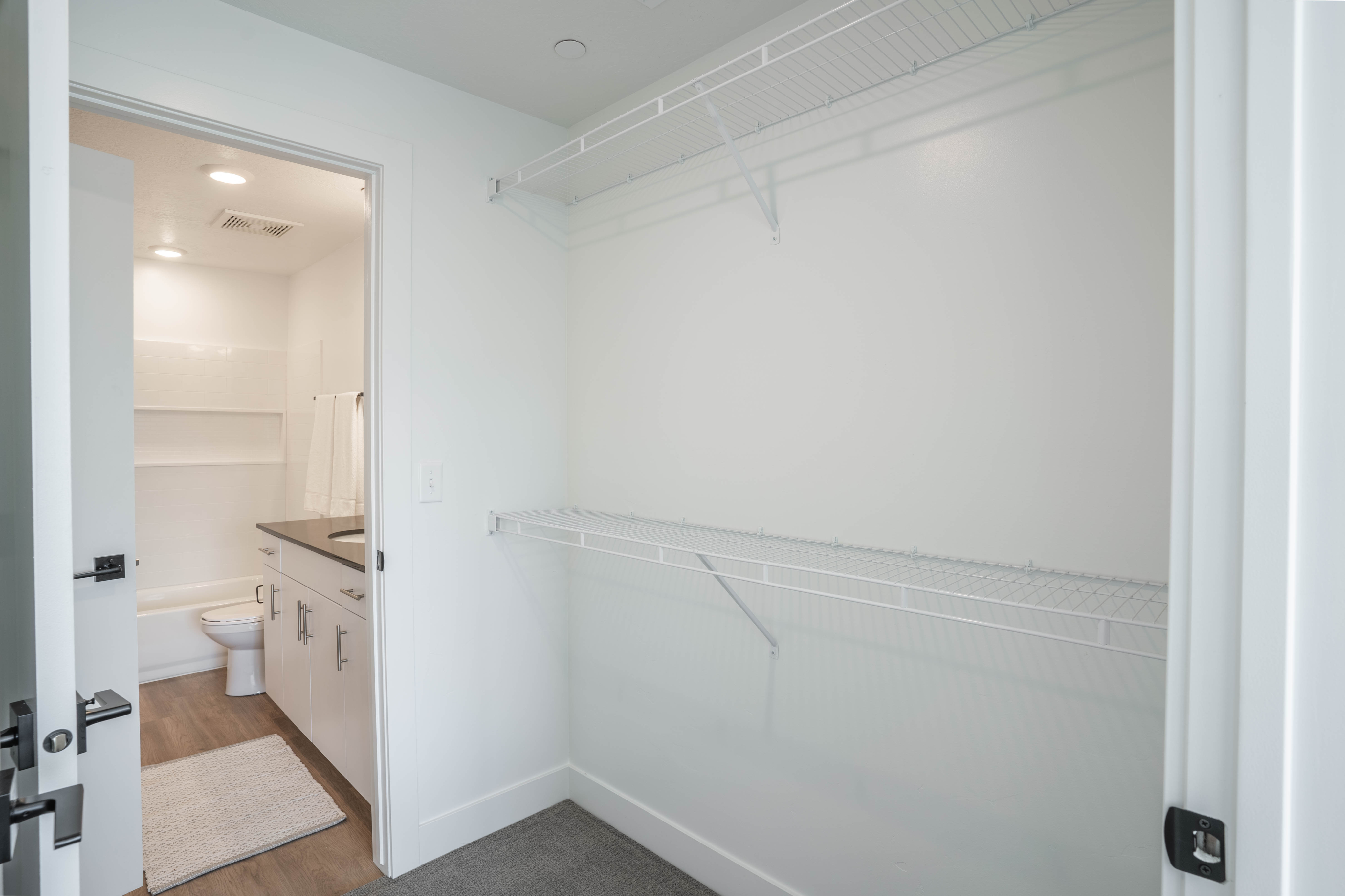Bright and clean walk-in closet with ample shelving, next to a modern bathroom featuring a sleek vanity and cozy bath area.