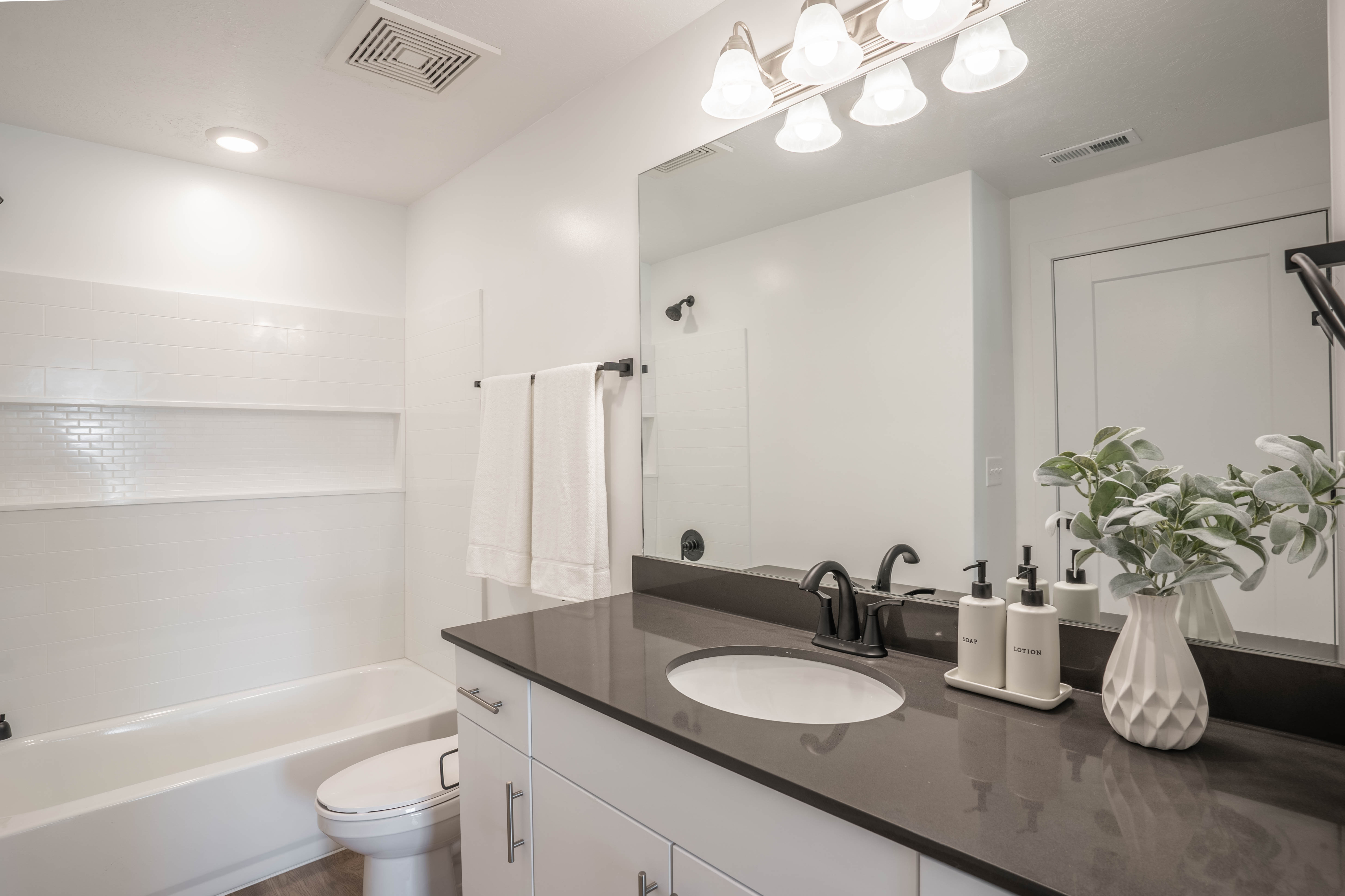 Elegant bathroom featuring a sleek vanity with a black countertop, modern fixtures, and stylish lighting. A cozy bathtub complements the bright and airy design with soft white tiles.