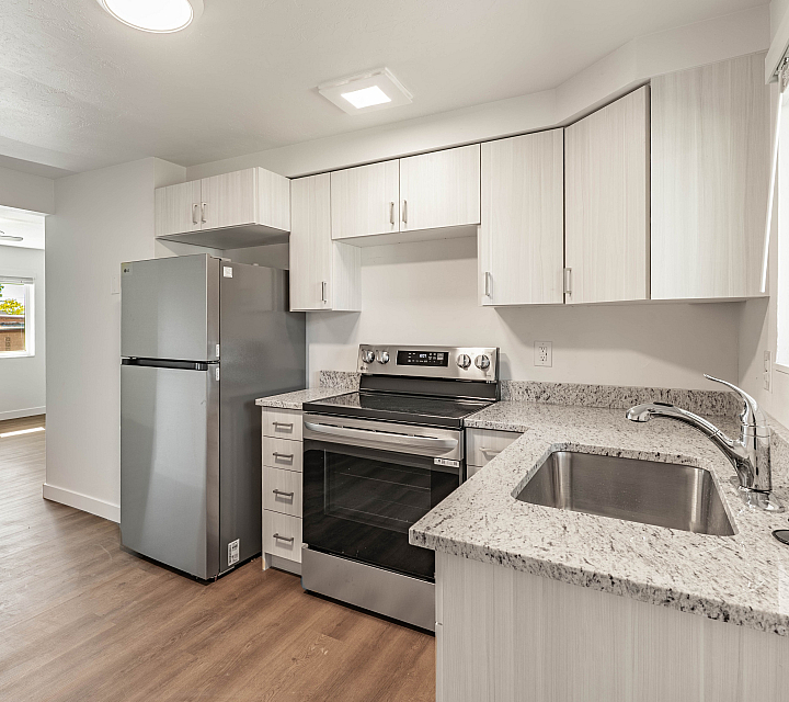 Modern kitchen with sleek stainless steel appliances, granite countertops, and abundant natural light connecting to a bright living area with large windows.