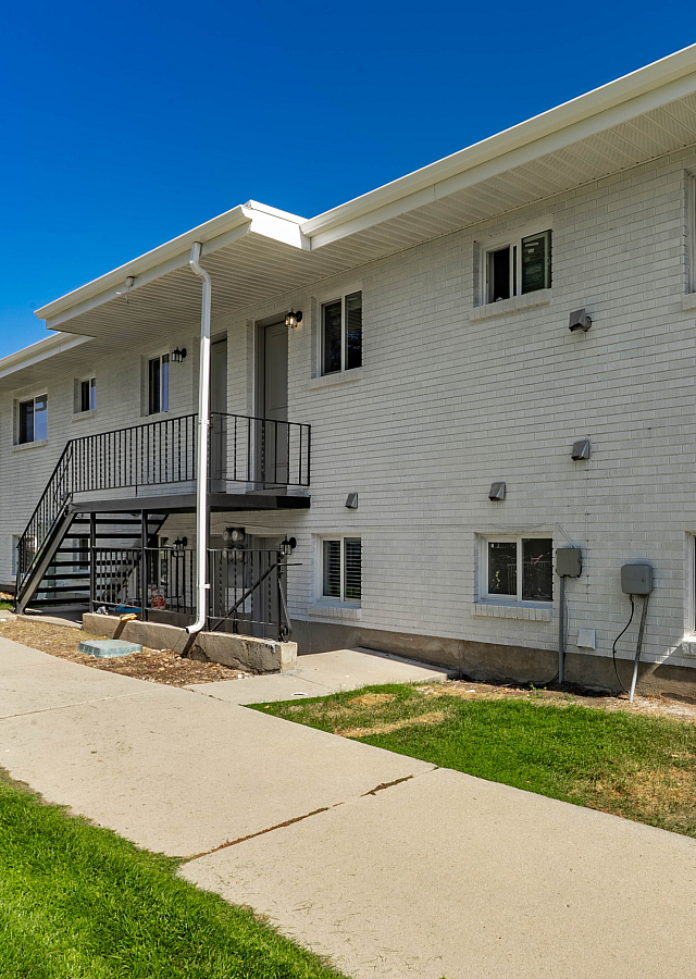 Charming apartment building with white brick exterior, landscaped lawn, and a welcoming pathway under a clear blue sky.