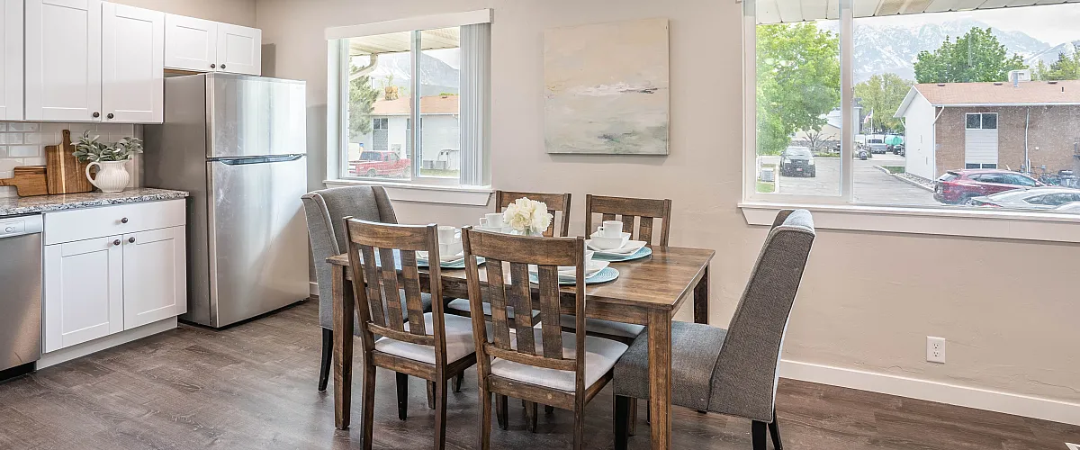 Bright, contemporary kitchen-dining area with modern white cabinetry, stainless steel appliances, and elegant wooden dining set, enhanced by natural light and scenic window views.