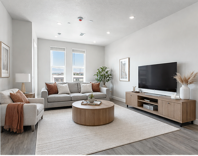 Bright and stylish living room featuring a modern gray sofa, large flat-screen TV, and sleek wooden furniture. Large windows allow natural light to illuminate the space beautifully.
