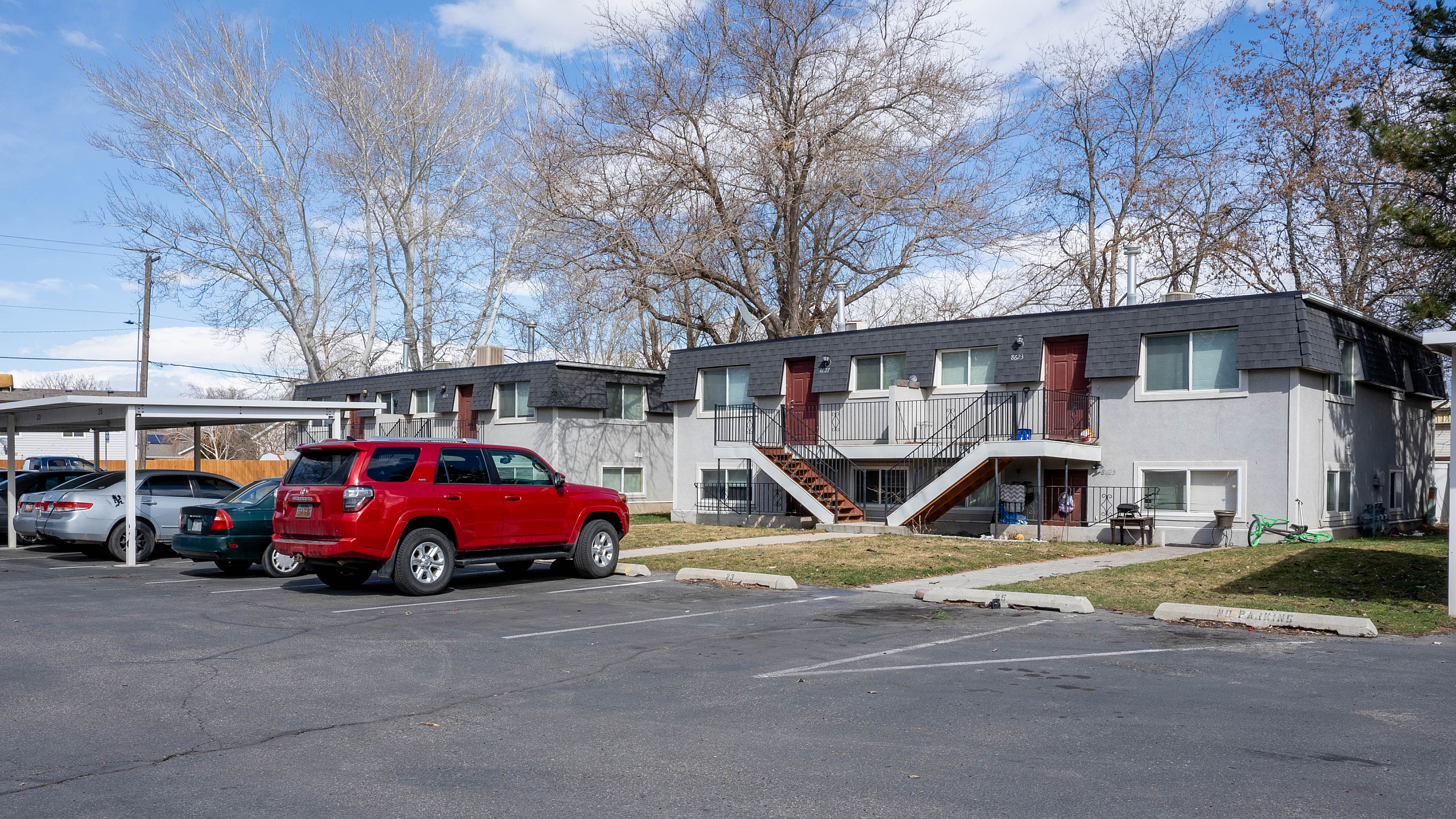 Charming residential apartment complex with well-maintained grounds, ample parking, and mature trees under a clear blue sky.